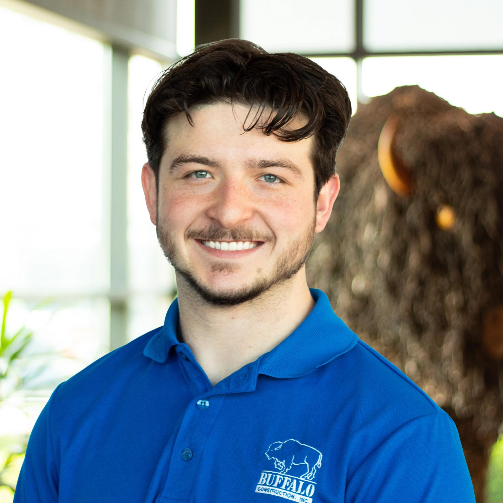 Nate Clark, smiling as he stands in front of a statue of a buffalo, wearing a royal blue Buffalo-branded polo.