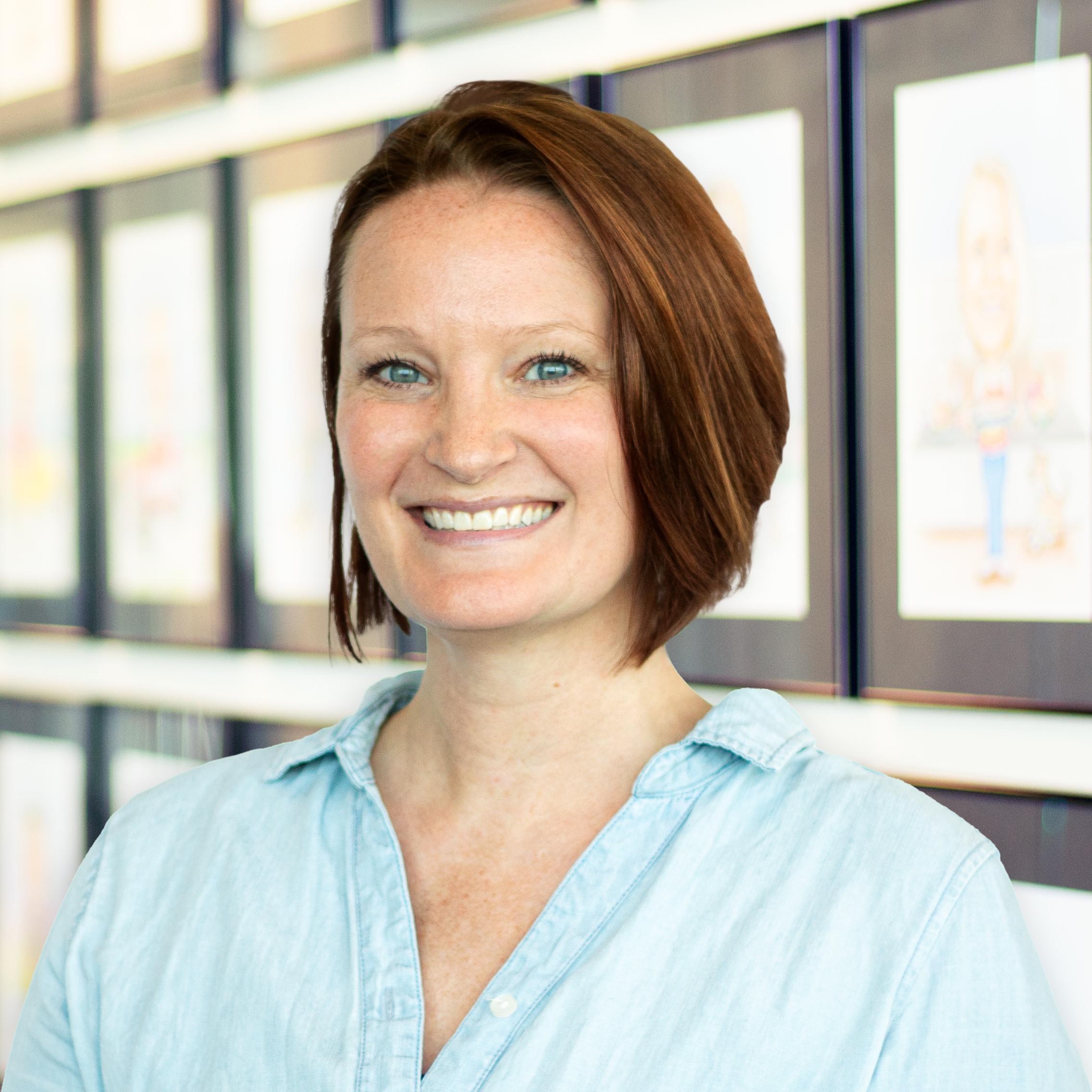 Erin Anderson wearing a smile, standing in front of a wall displaying framed caricatures.