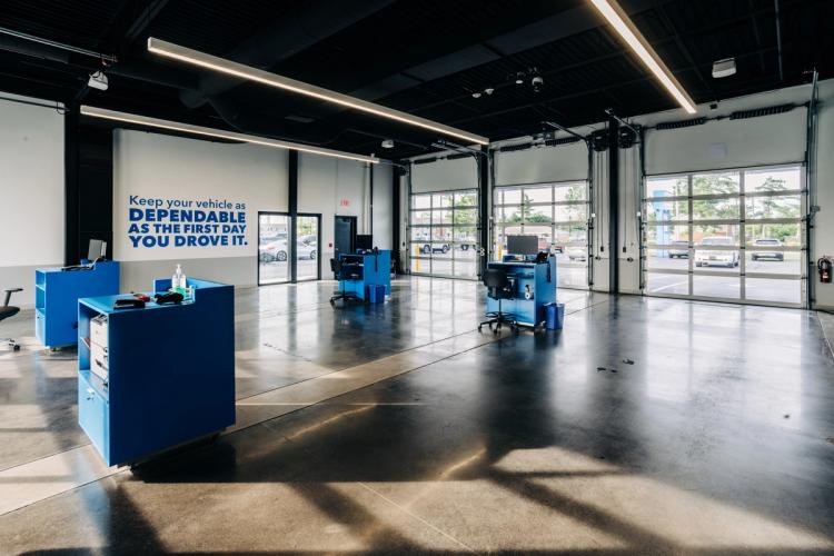 Completed automotive service bay featuring polished concrete floors, blue service stations, glass overhead doors and linear ceiling lights.
