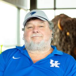Jim Sanders wearing a UK polo as they stand in front of a statue of a buffalo.