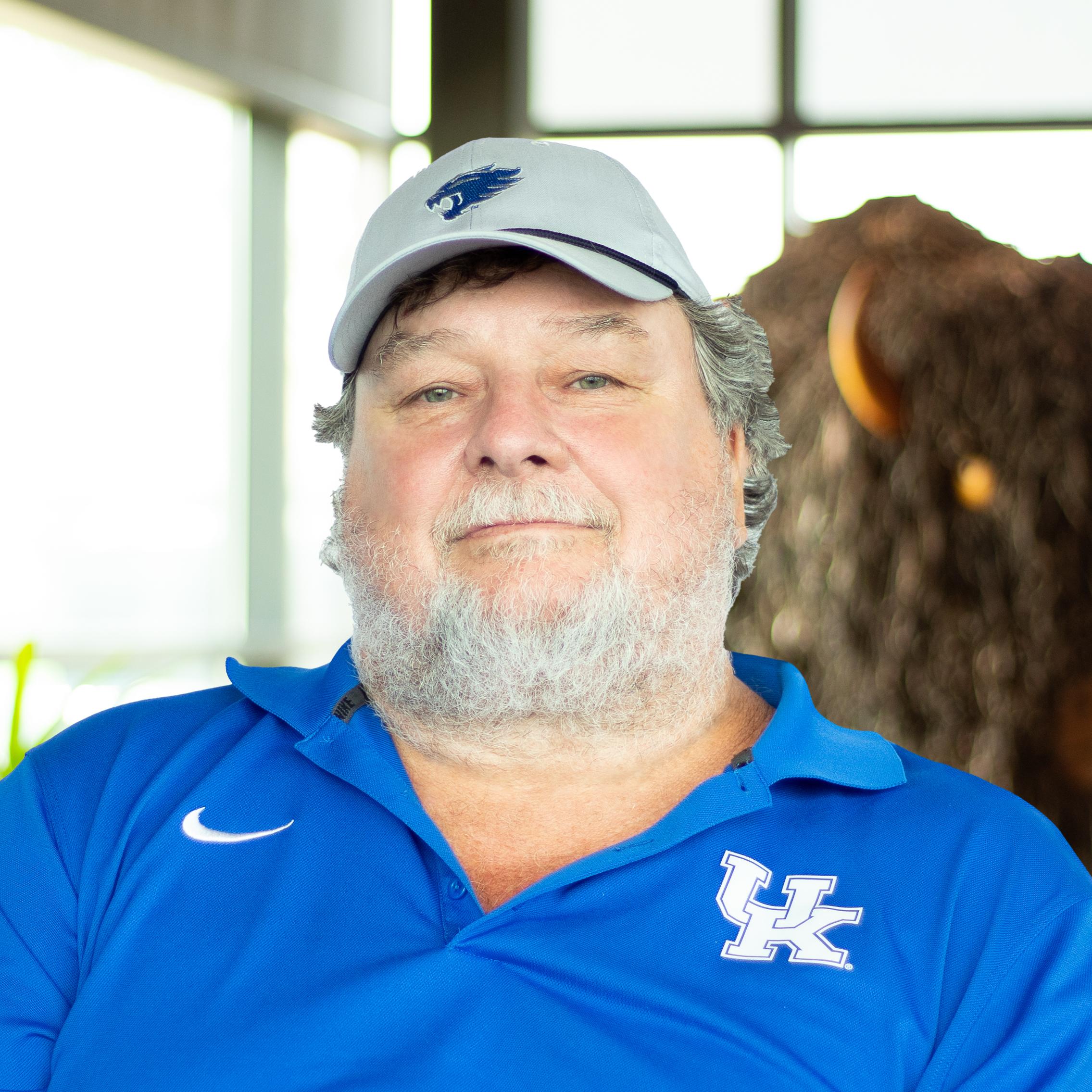 Jim Sanders wearing a UK polo as they stand in front of a statue of a buffalo.