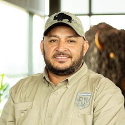 Armando Gomez smiling as he stands proudly in front of a statue of a buffalo.