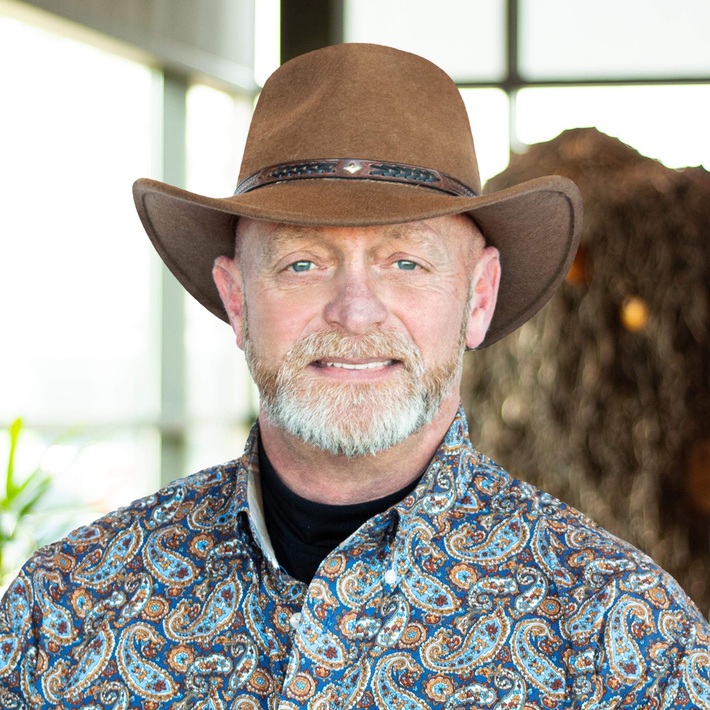 Tony Baker in a brown cowboy hat, wearing a smile as he stands in front of a statue of a buffalo.