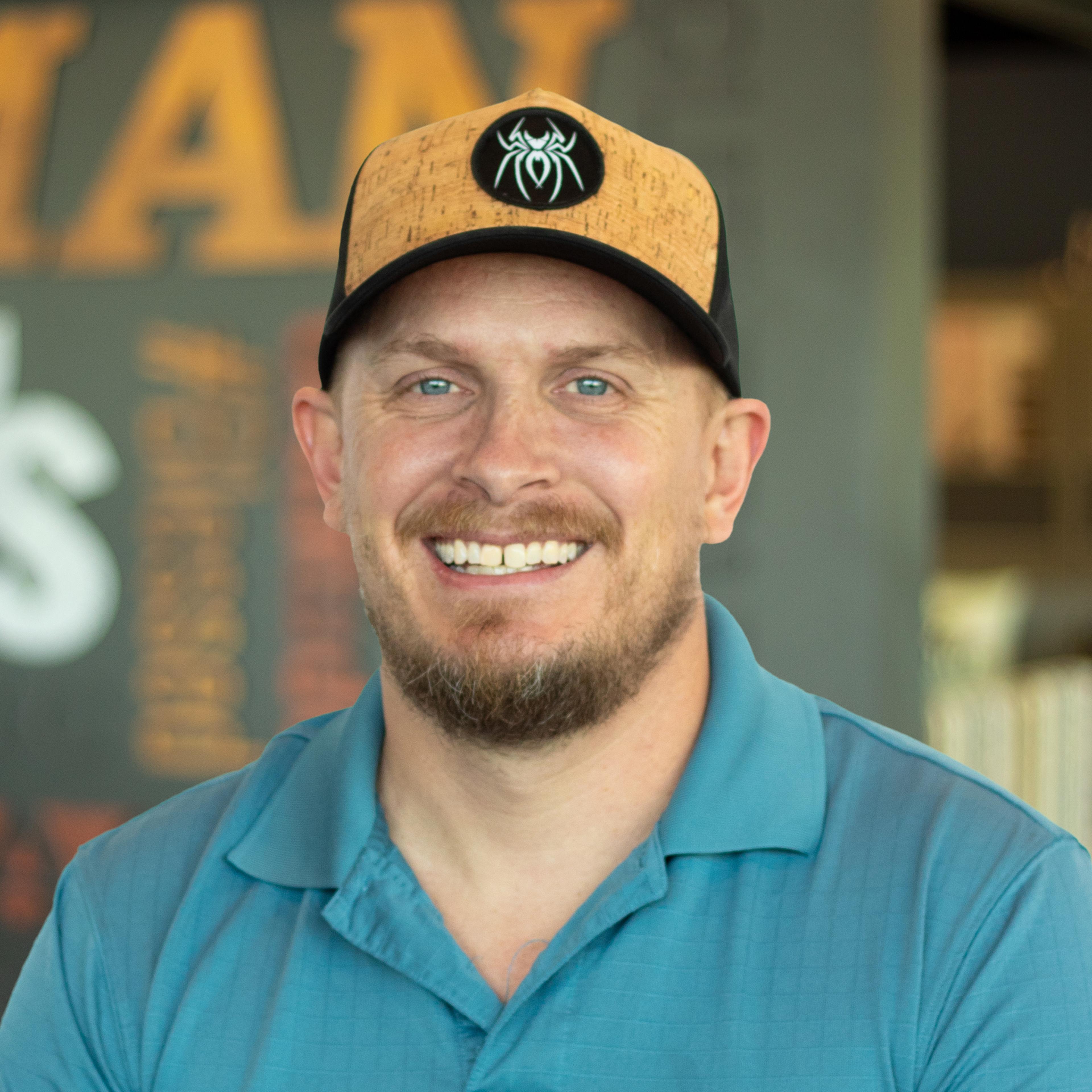 Kyle Ashley smiling, wearing a teal polo shirt and cap, standing in Buffalo Construction's office space.