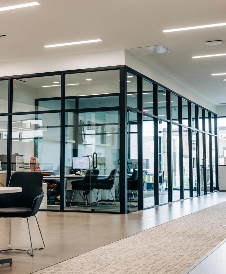 Completed dealership interior featuring black-framed glass offices, modern lighting, customer seating and light wood flooring.