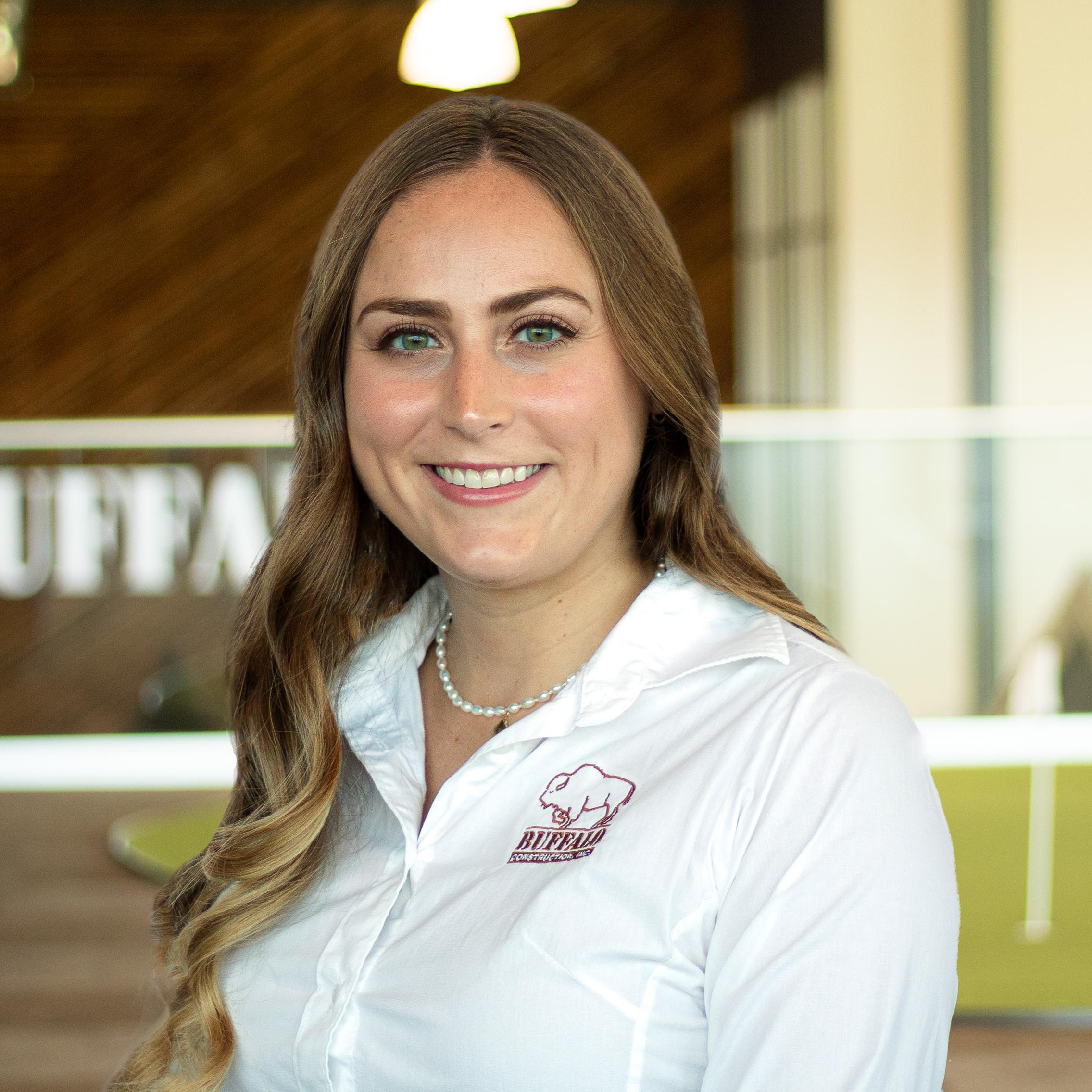 Maddie Sturgeon smiling, wearing a buffalo branded button down shirt , standing in buffalo's office space.