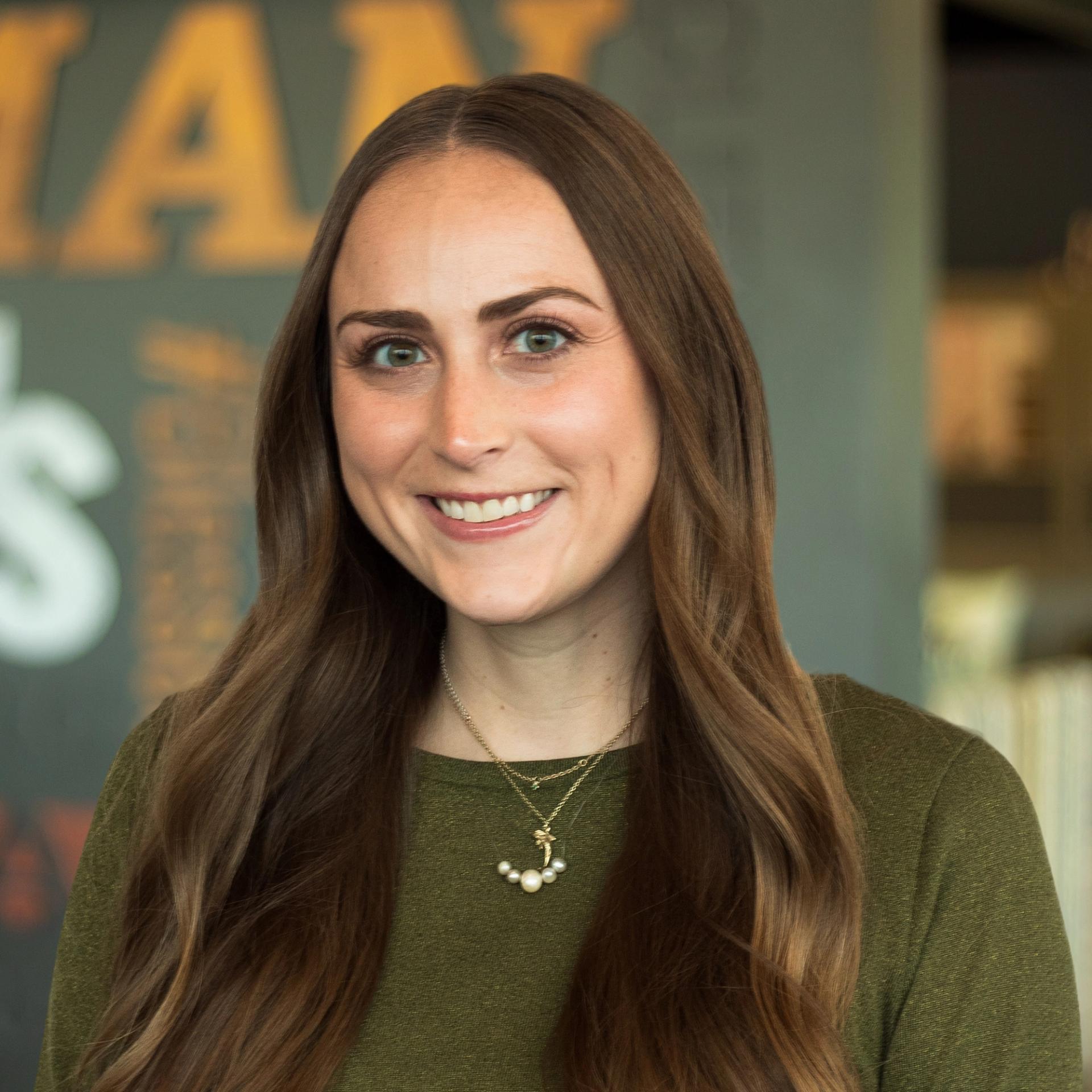 Maddie Sturgeon wearing a green top and necklace and standing in front of a company-branded wall.