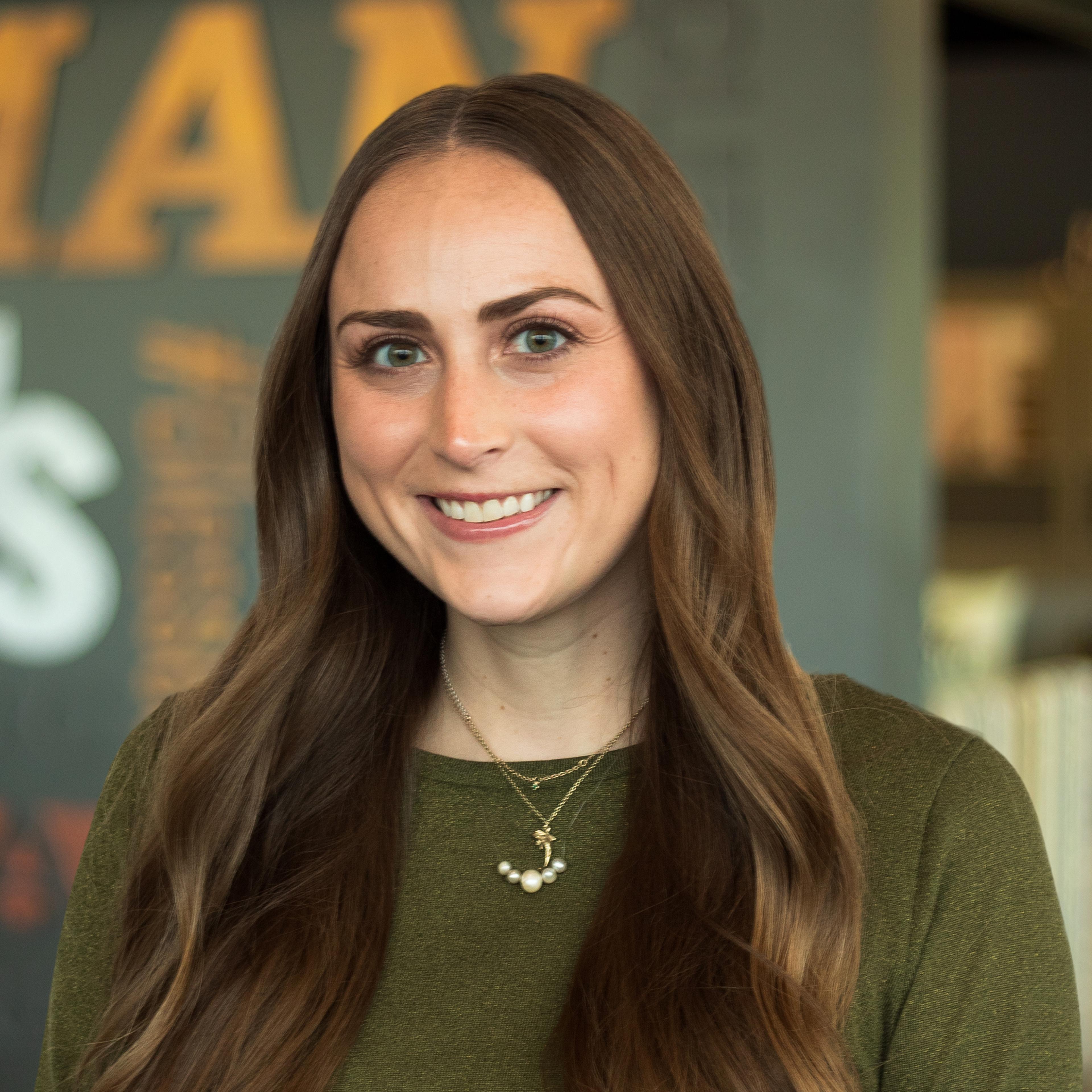 Maddie Sturgeon wearing a green top and necklace and standing in front of a company-branded wall.