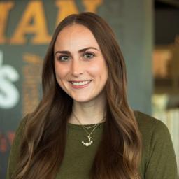 Maddie Sturgeon wearing a green top and necklace and standing in front of a company-branded wall.