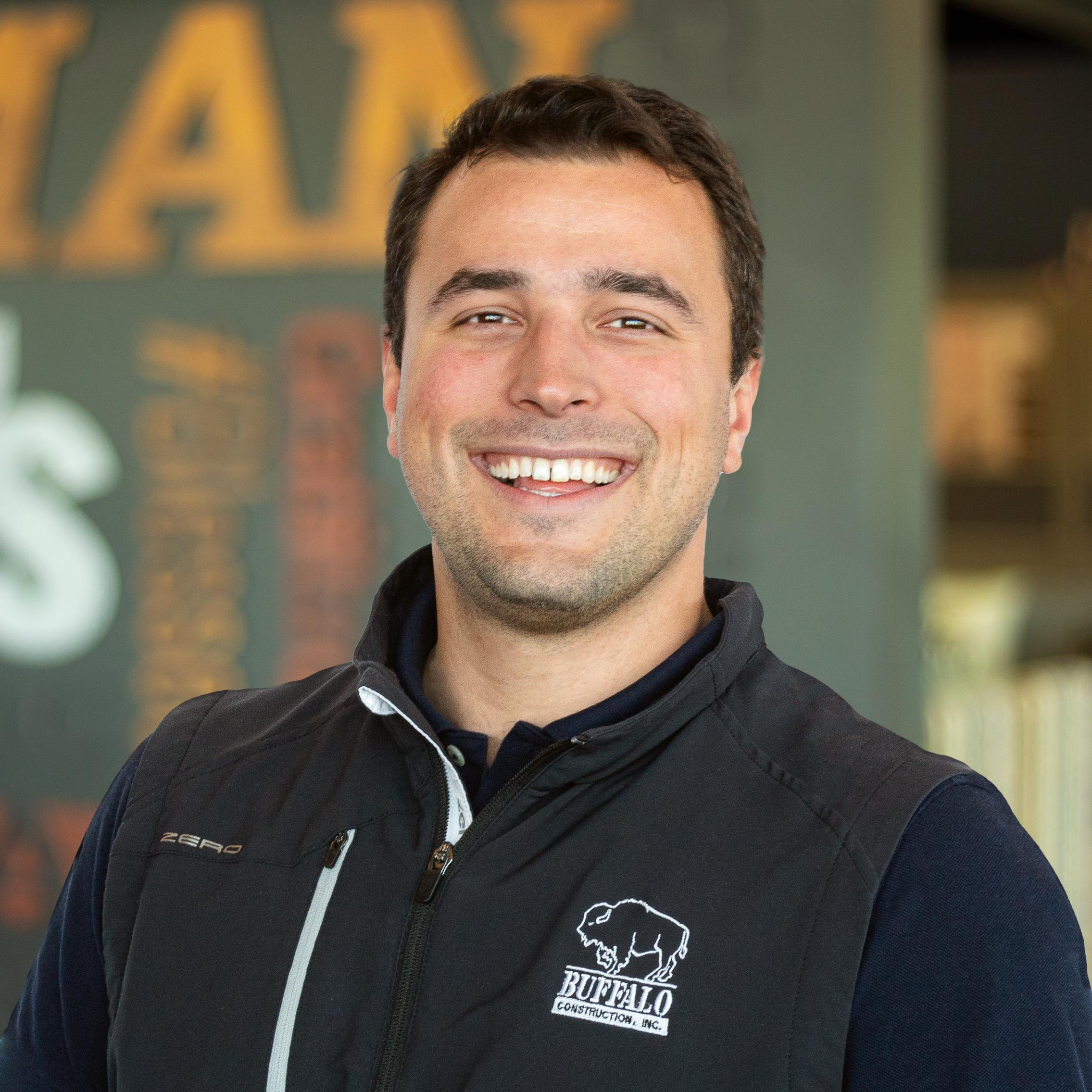 Gio Giorcelli wearing a buffalo branded vest and smiling in front of a company-branded wall.