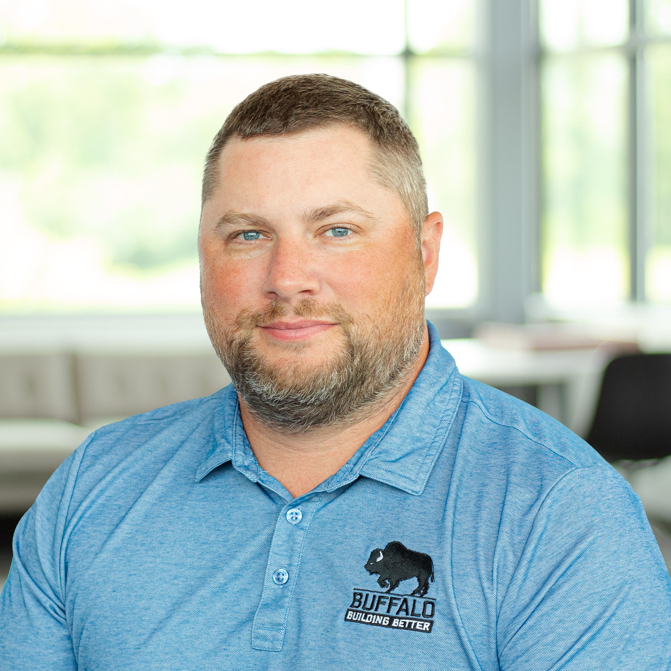 Tim Fishburn wearing a light blue buffalo branded polo, in a bright, modern office.
