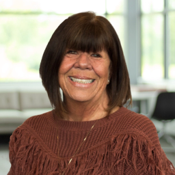 Carol Stokes wearing a brown sweater, smiling in a bright, modern office.