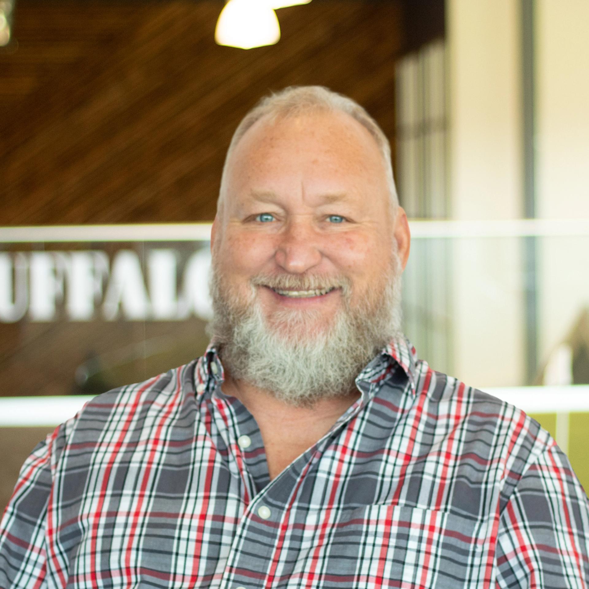 Harold Temple wearing a plaid button-down shirt, smiling in a bright, modern office.