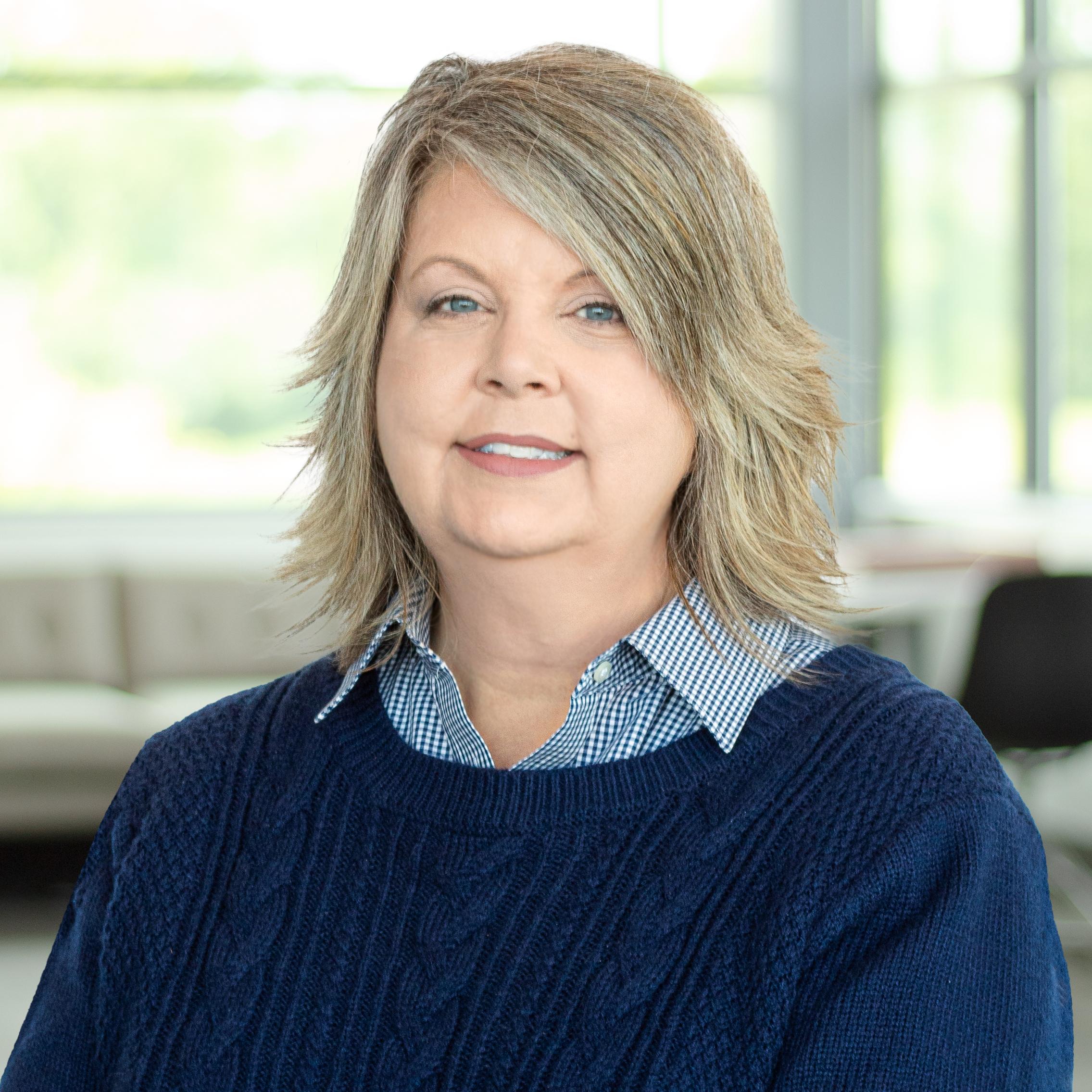 Teresa Parsons wearing a navy blue sweater and smiling in a bright, modern office.