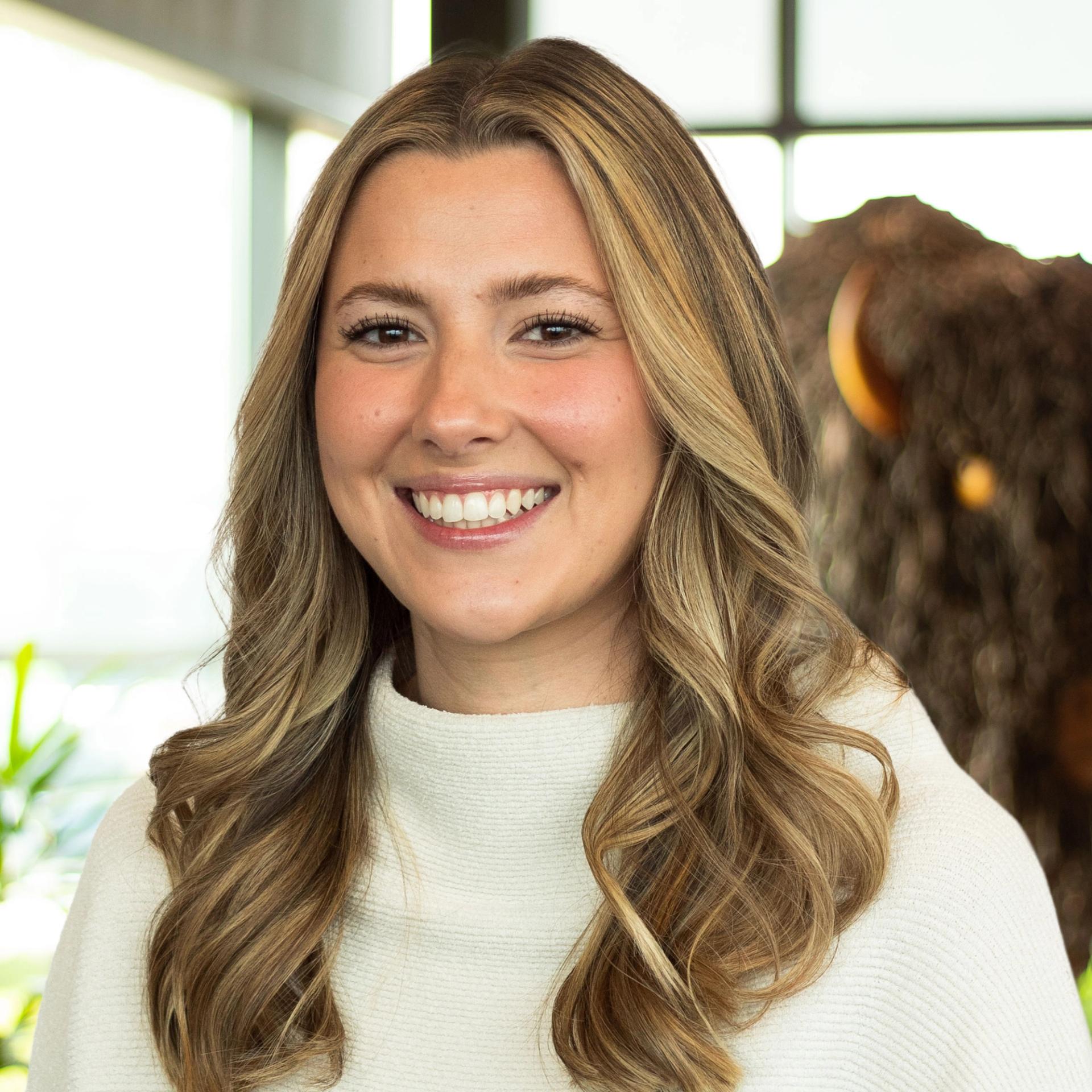 Josie Hornback smiling, wearing a light sweater, standing in front of a buffalo statue in the office.