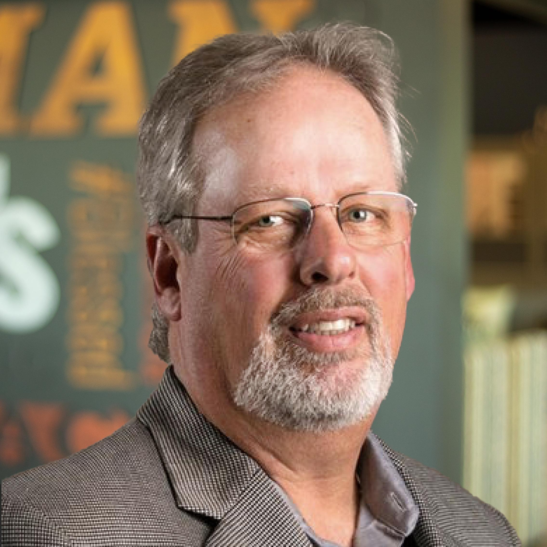 Charlie Evans smiling and standing in front of a company-branded wall.