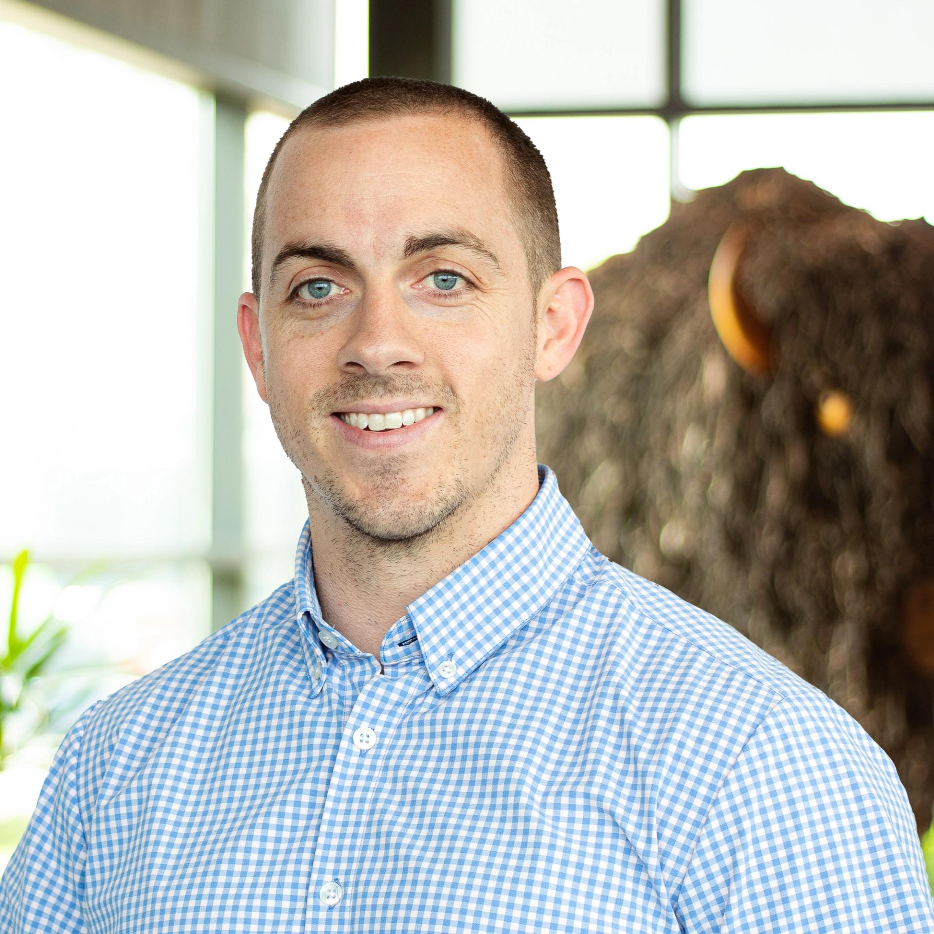 Dan Burke smiling as they stand in front of a statue of a buffalo.