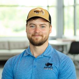 Scott Messer wearing a blue buffalo construction branded polo, smiling in a bright, modern office.