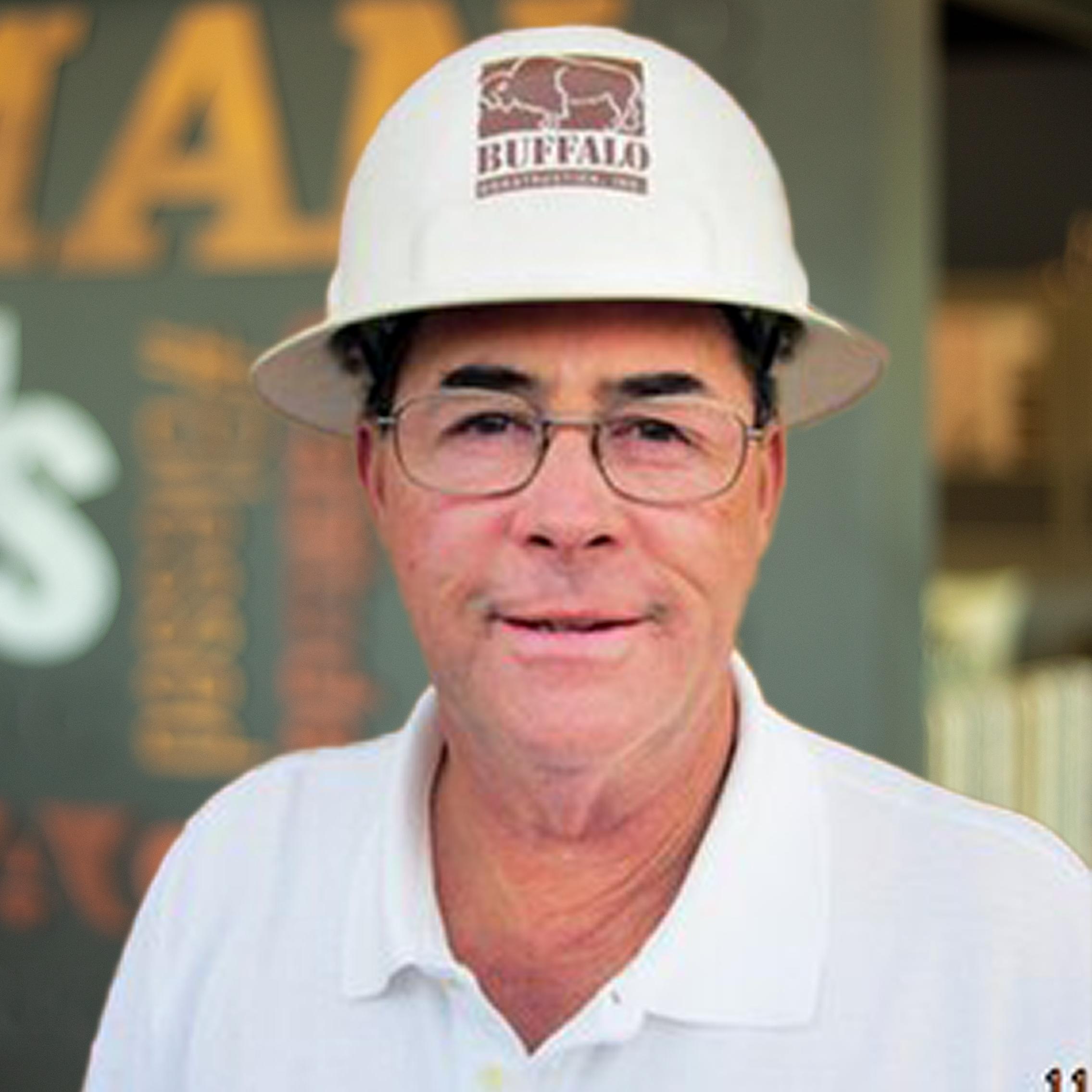 Don Johnson proudly wearing a buffalo construction hard hat, standing in front of a company-branded wall.