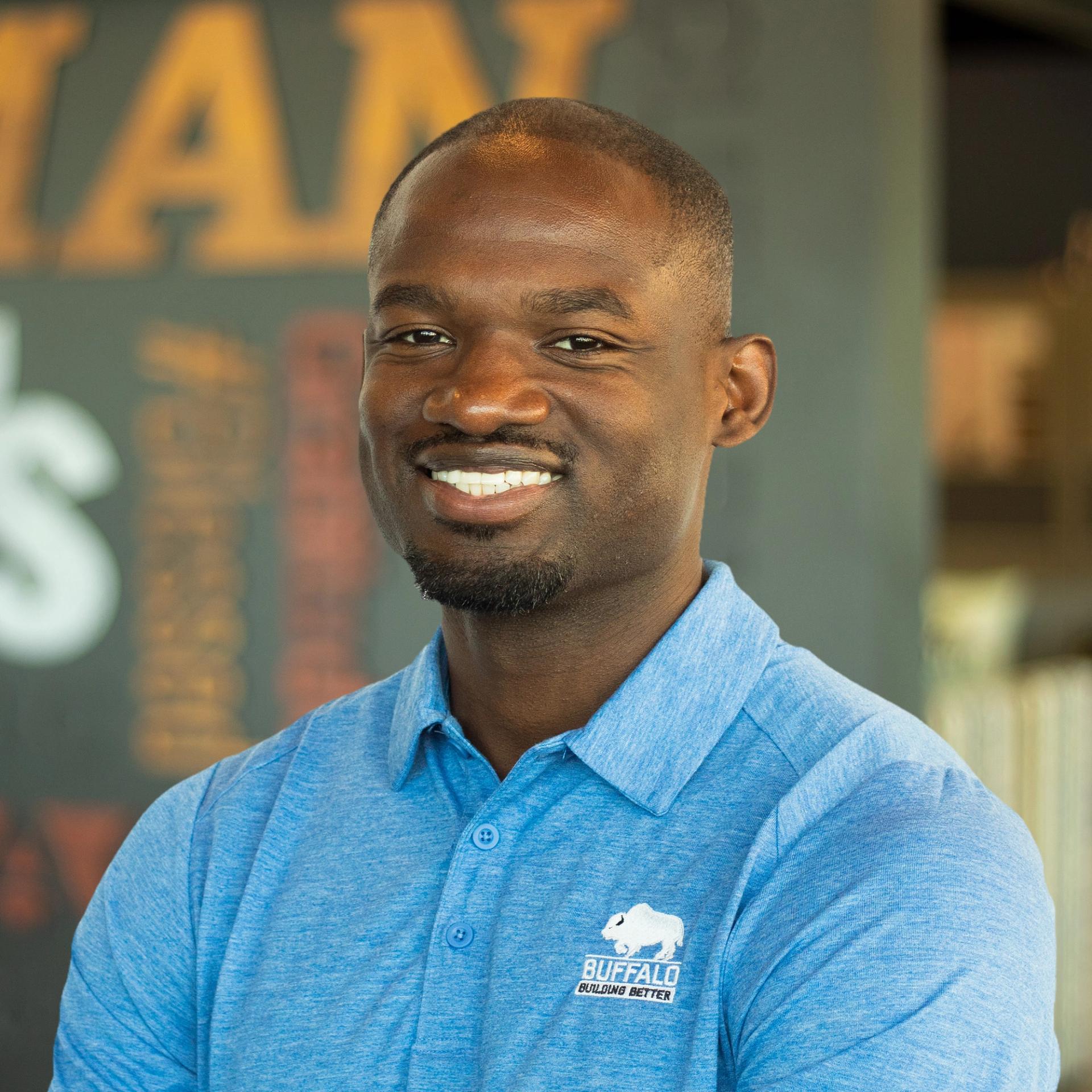 Jordon Johnson smiles while wearing a blue Buffalo Construction polo, standing in front of a company-branded wall.