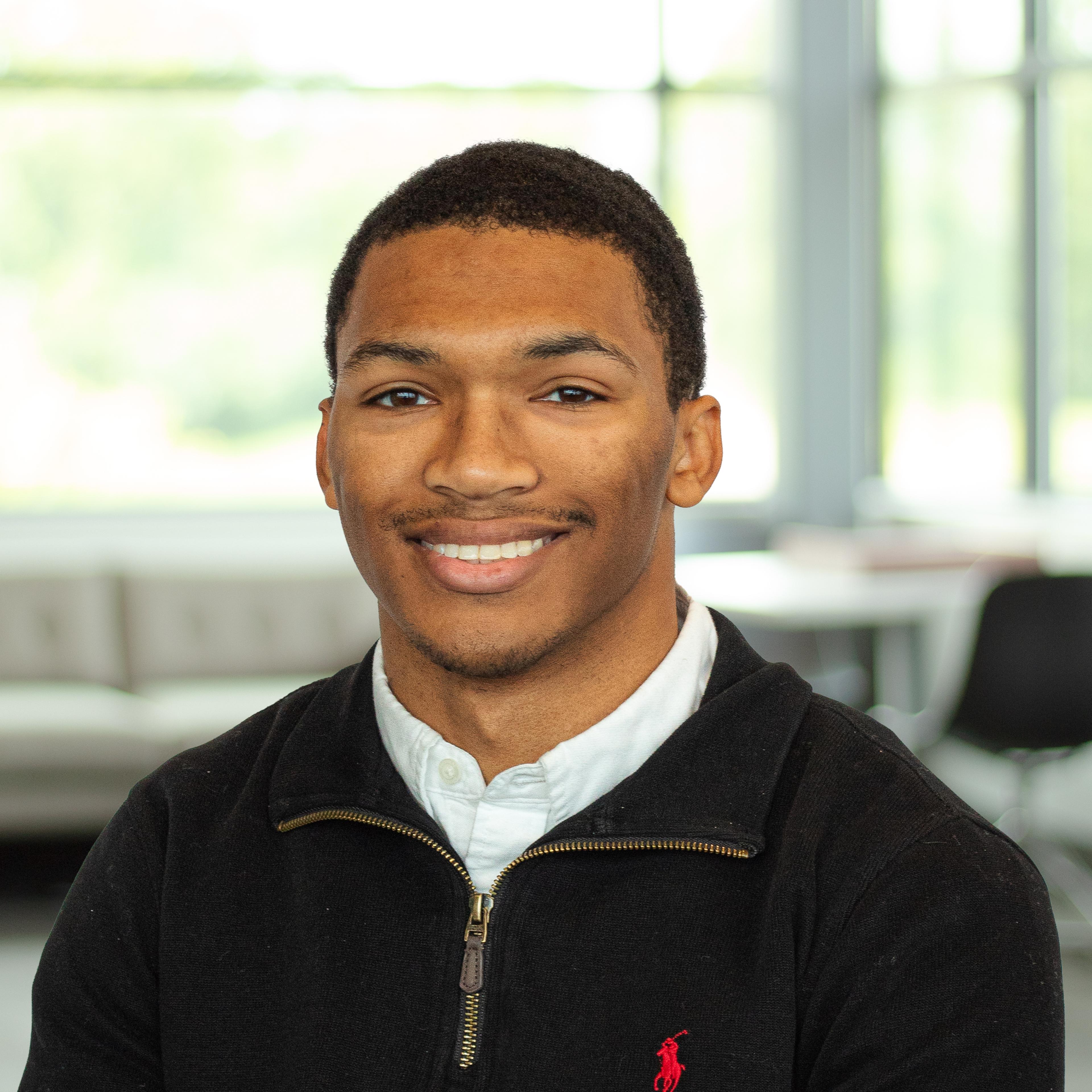 Caleb Griggs wearing a black sweater with a white shirt, smiling confidently in a bright, modern office.