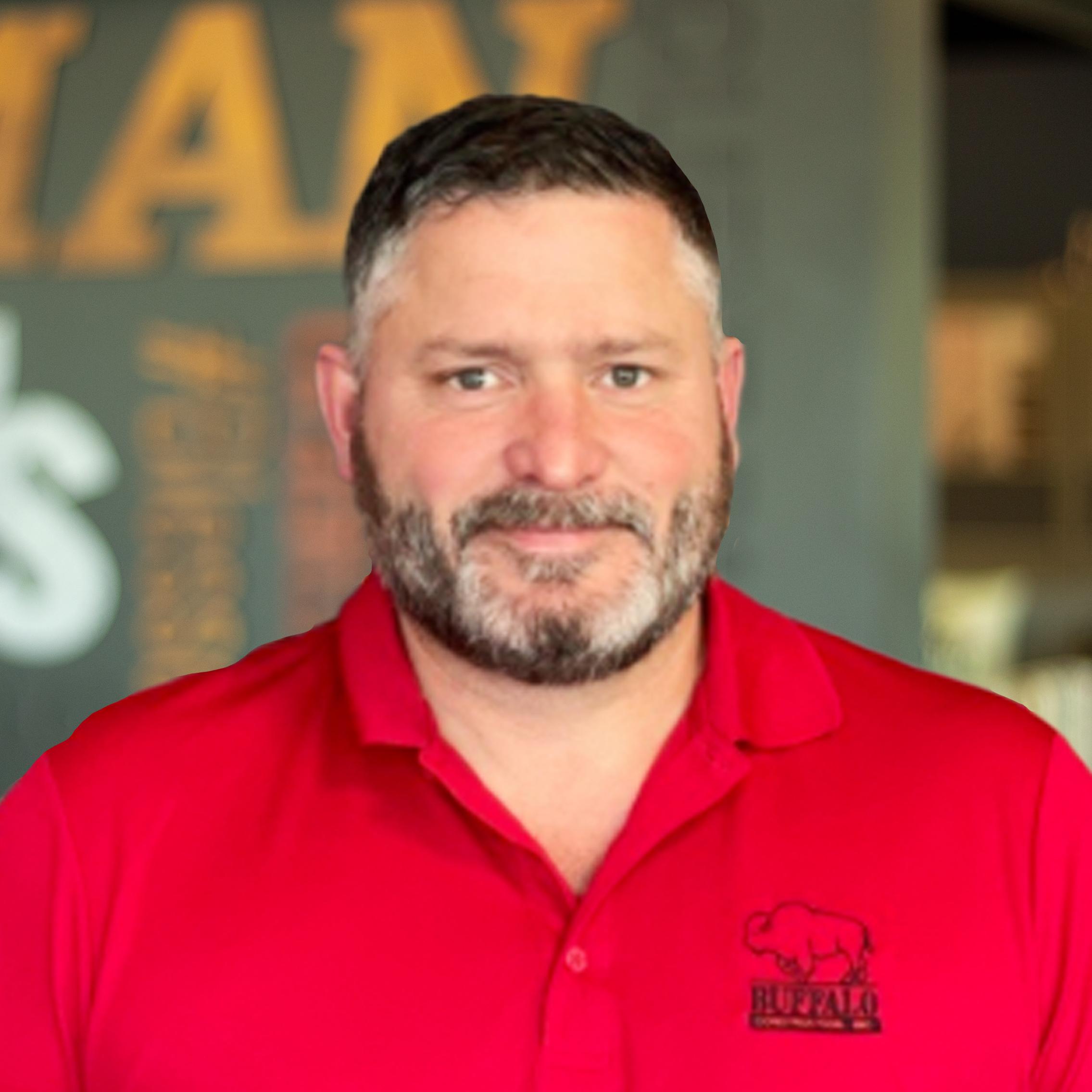 Aaron Bixby giving a slight smile, in a red buffalo branded polo, standing in front of a company-branded wall.