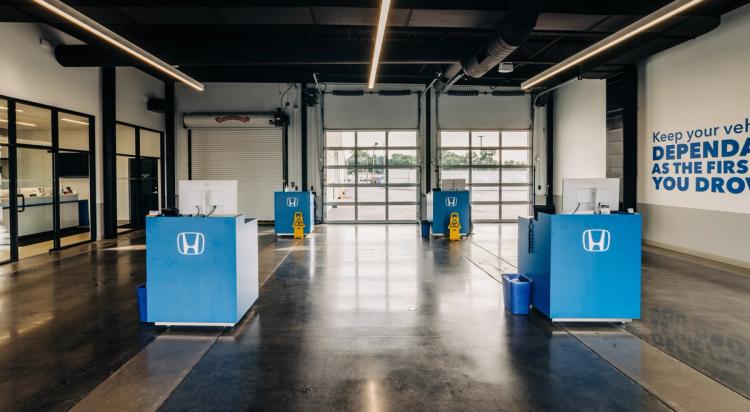 Completed Honda service bay with four blue technician workstations, polished concrete flooring and overhead vehicle doors.