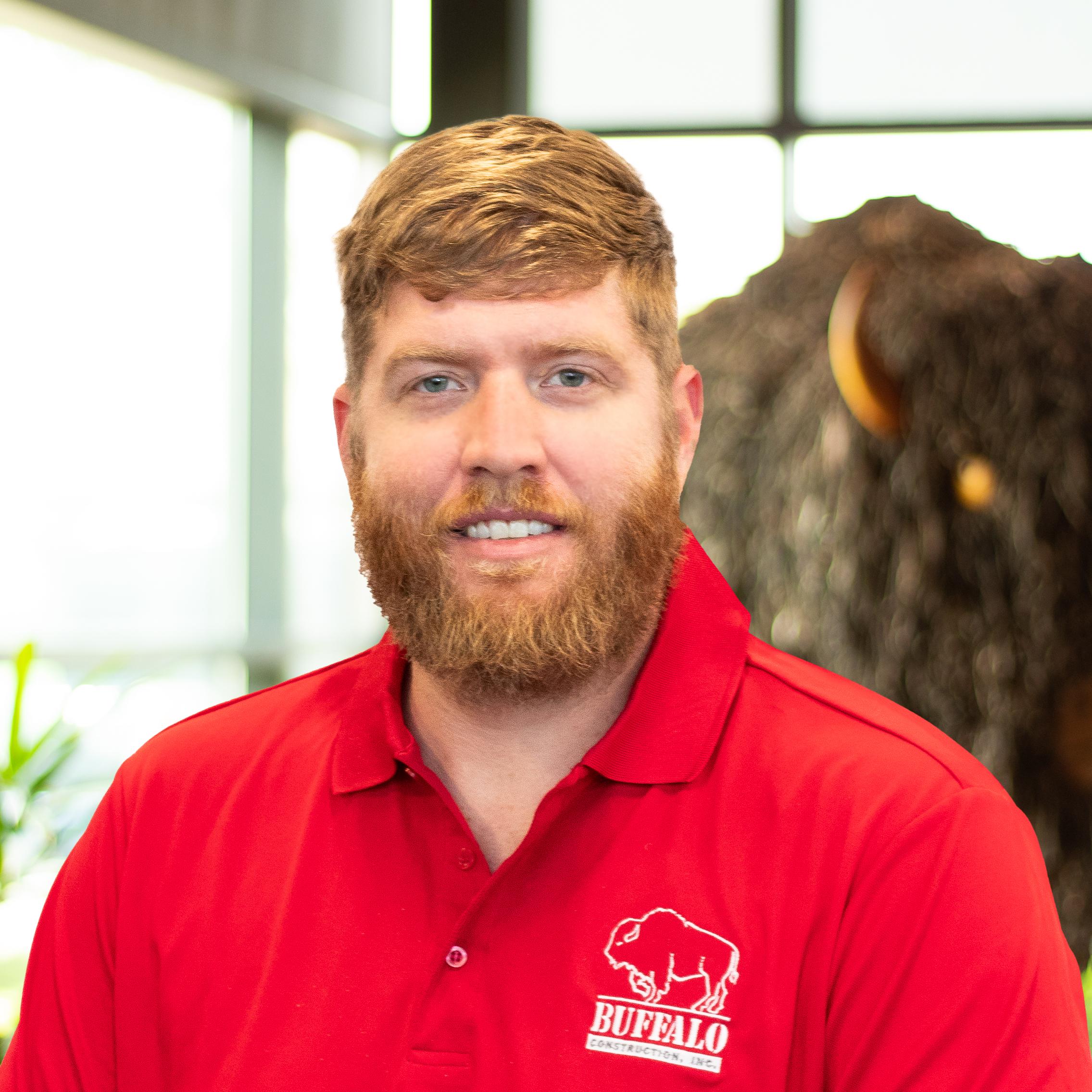Zach Fields, wearing a red buffalo branded polo as they stand in front of a statue of a buffalo.