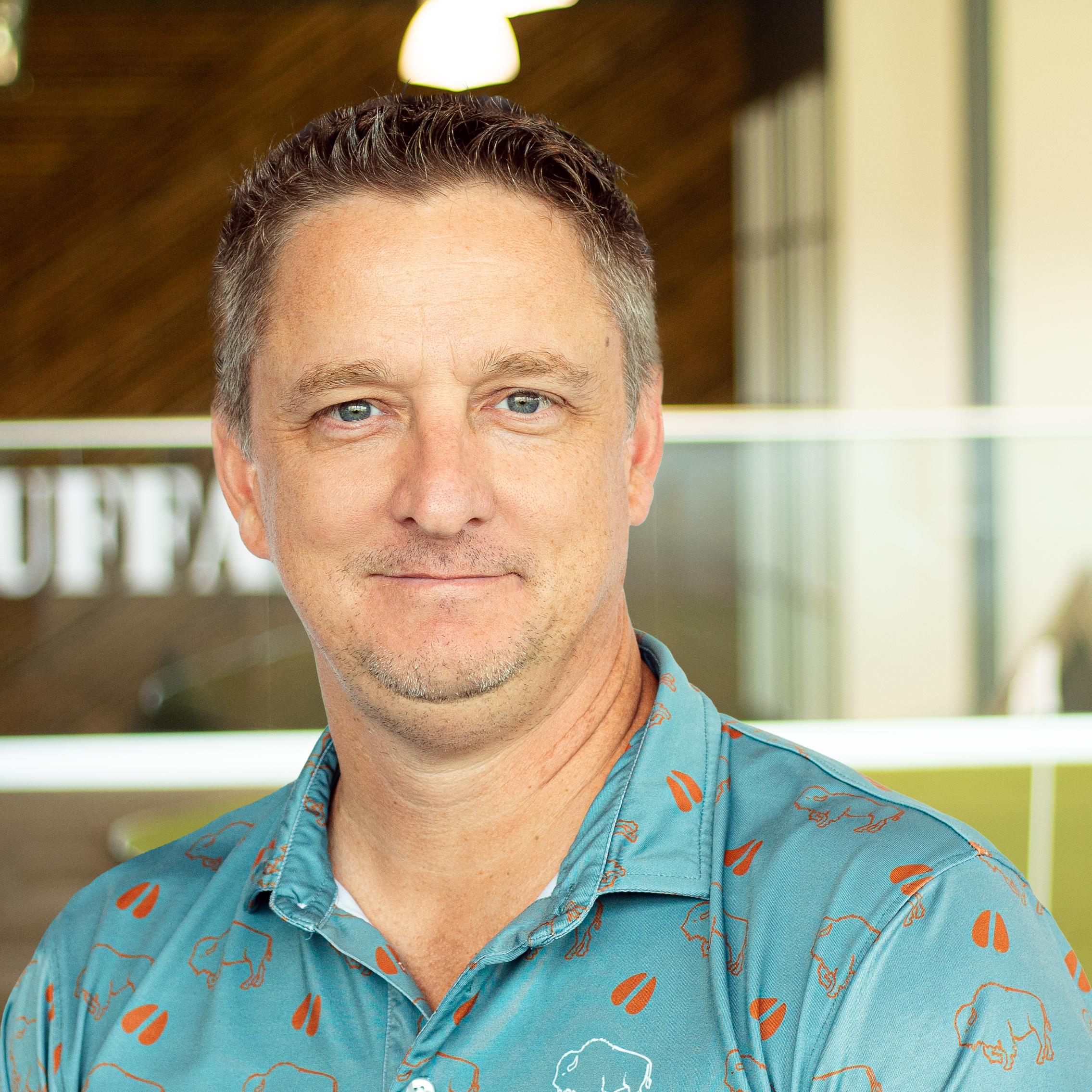 Chris French with a slight smile, wearing a buffalo branded polo, standing in buffalo's office space.