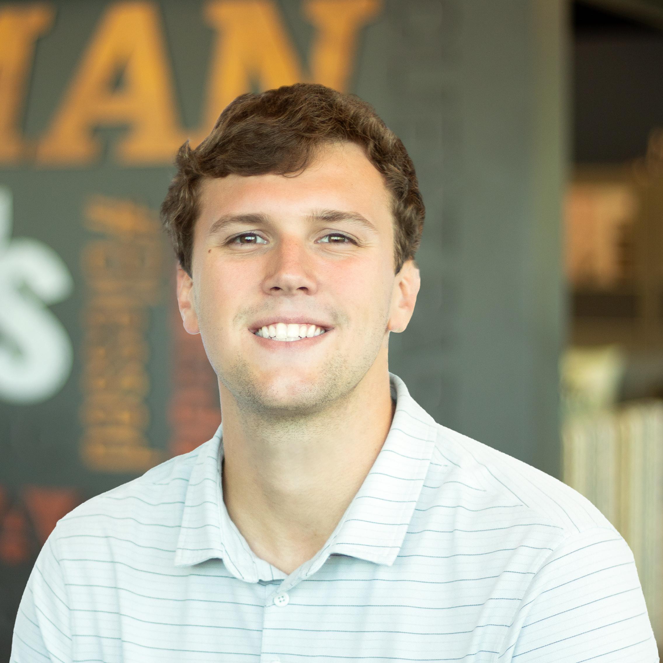 Ben Taylor wearing a polo and standing in front of a company-branded wall.