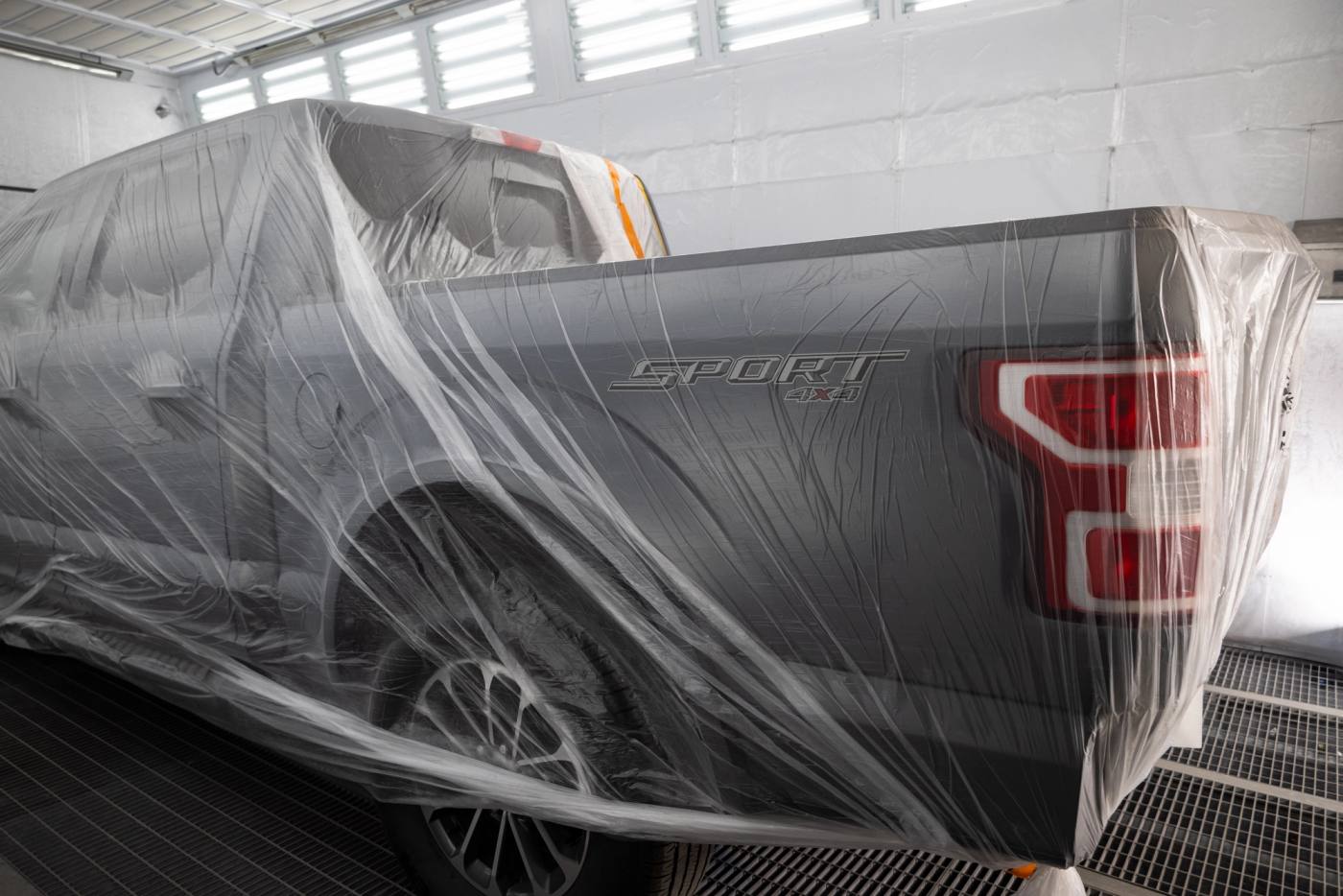 A grey Ford F-150 pickup wrapped in protective film, prepped in a Carl's Collision paint booth