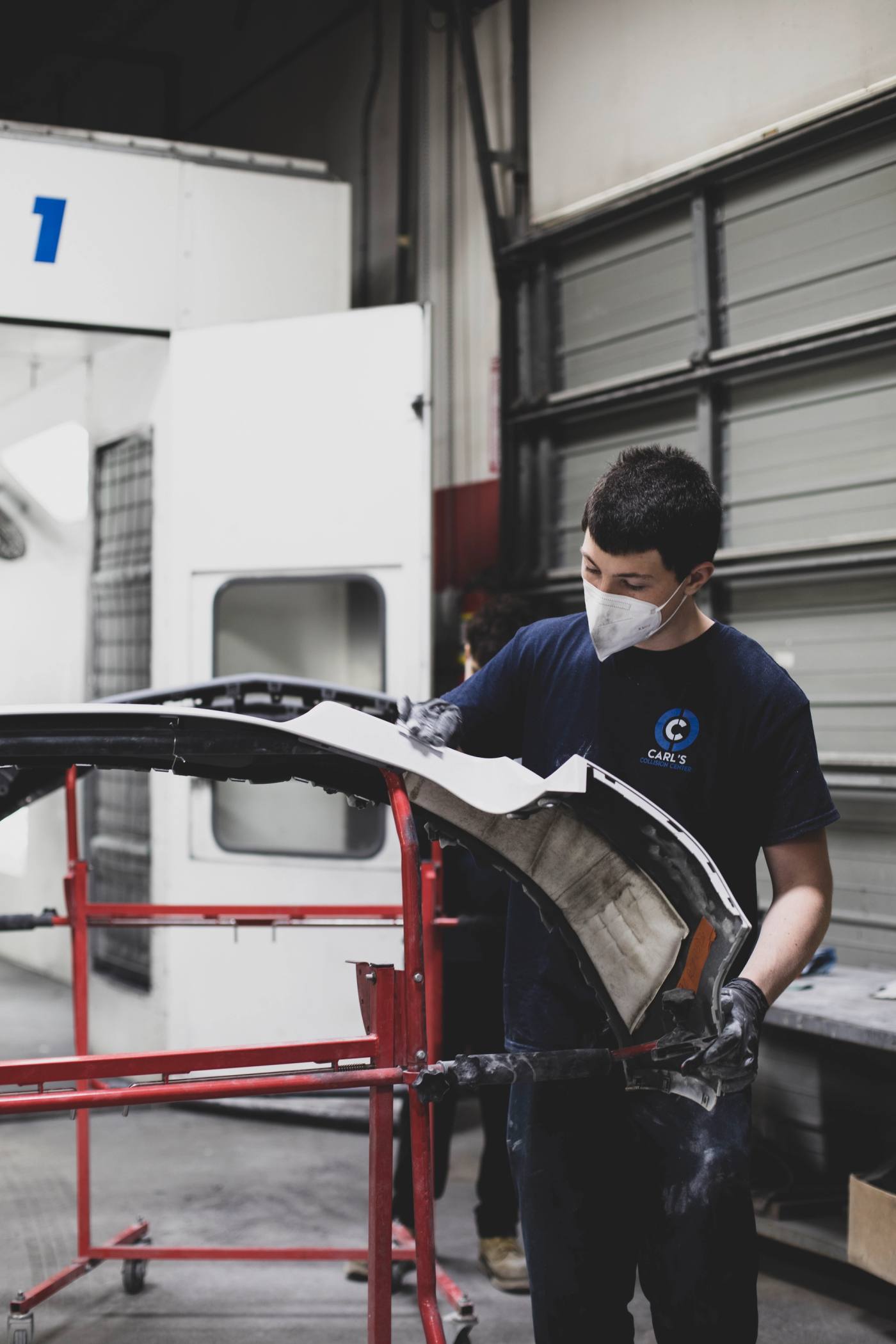 A Carl's Collision technician sanding a bumper cover in the prep booth