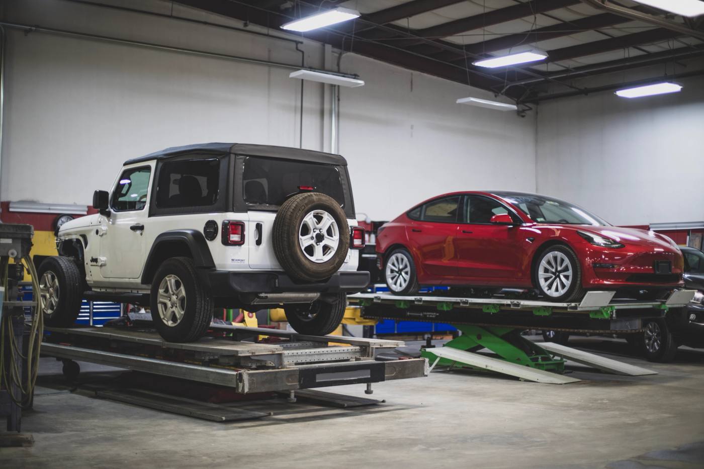 A Jeep Wrangler and a Tesla Model 3 on frame racks in the shop