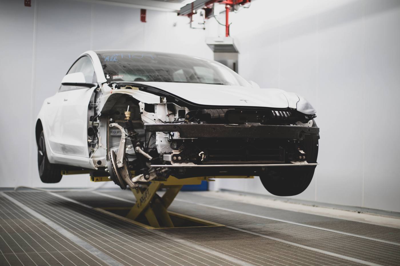 A white Tesla Model 3 with its front end disassembled during teardown