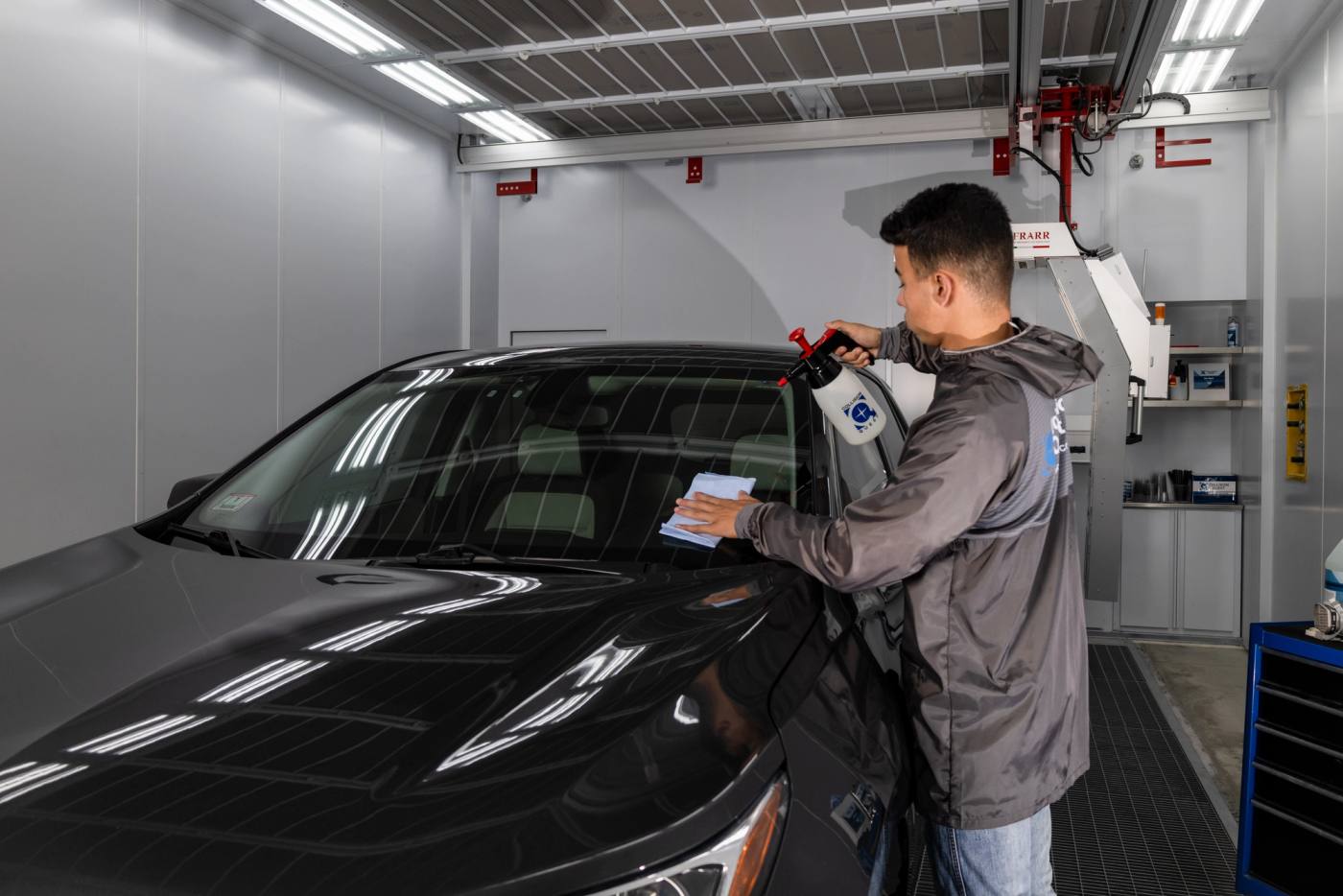 A technician using a paint color-match tool on a black sedan