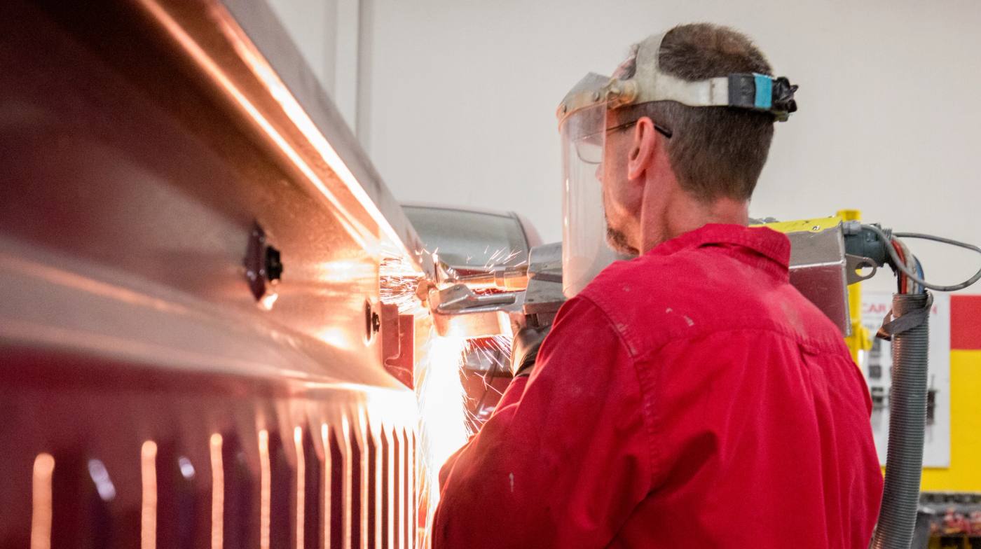 An auto body technician welding a panel with sparks flying