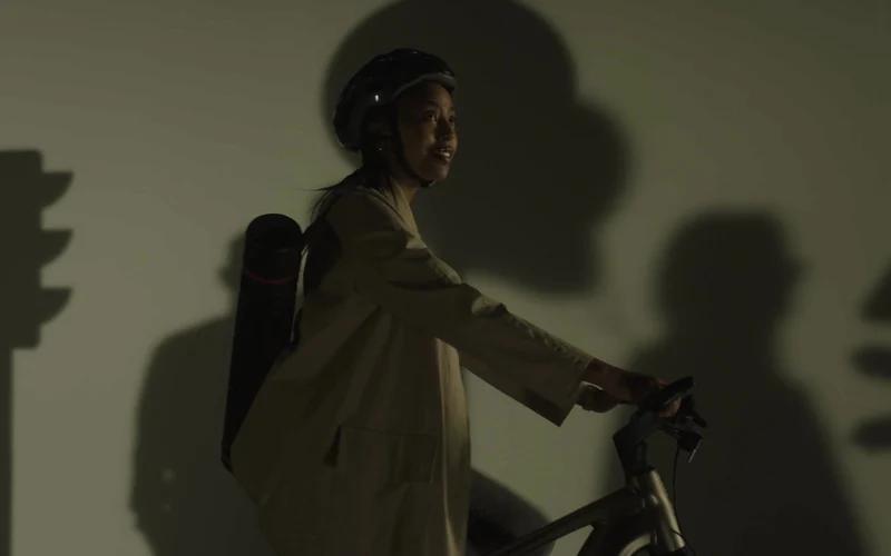 A helmeted cyclist turns towards the light as her shadow falls across a wall.