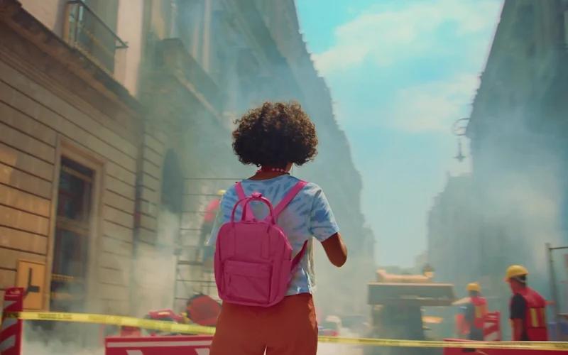 A roller-skater with a pink backpack looks into a sunlit city street.
