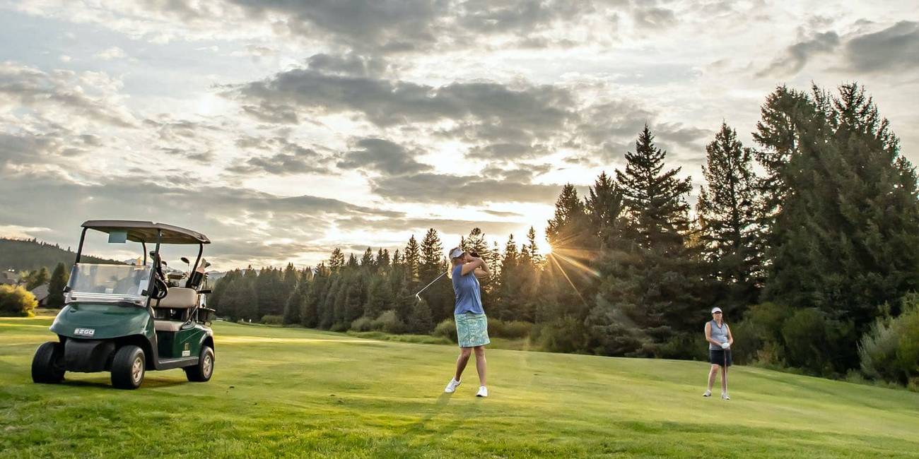 A golfer taking a swing on a golf course while another watches.