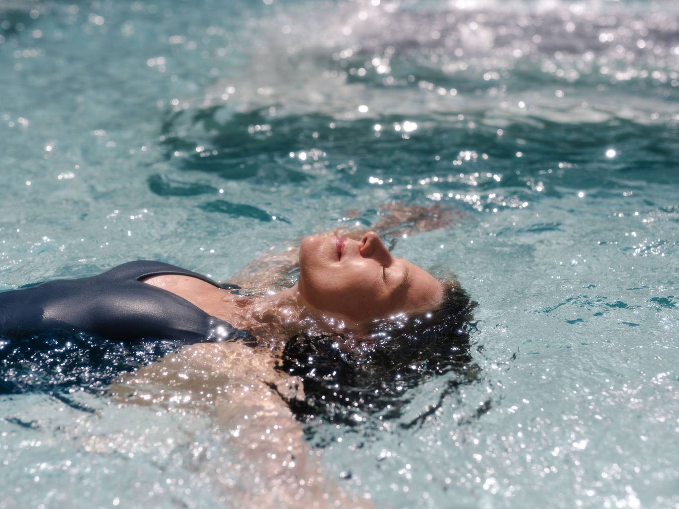 A lady floating on her back, looking very peaceful, in a pool.