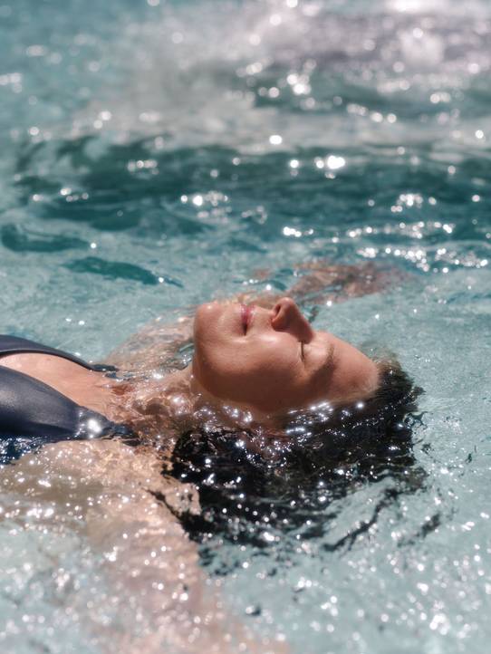 A lady floating on her back, looking very peaceful, in a pool.