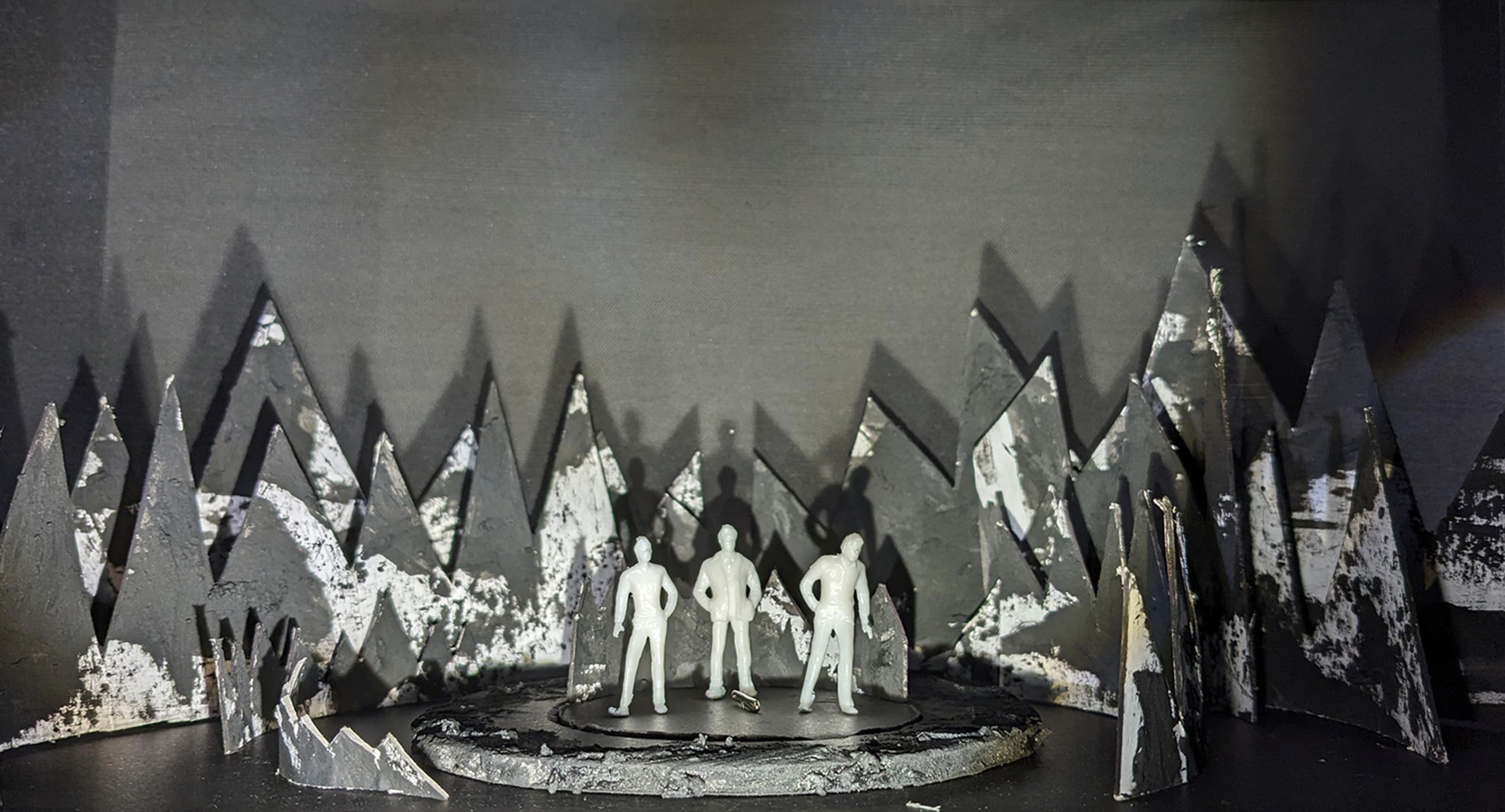 Scale model of a set design featuring jagged, mountainous black shapes in the background with small white figures positioned around a central circular stage.