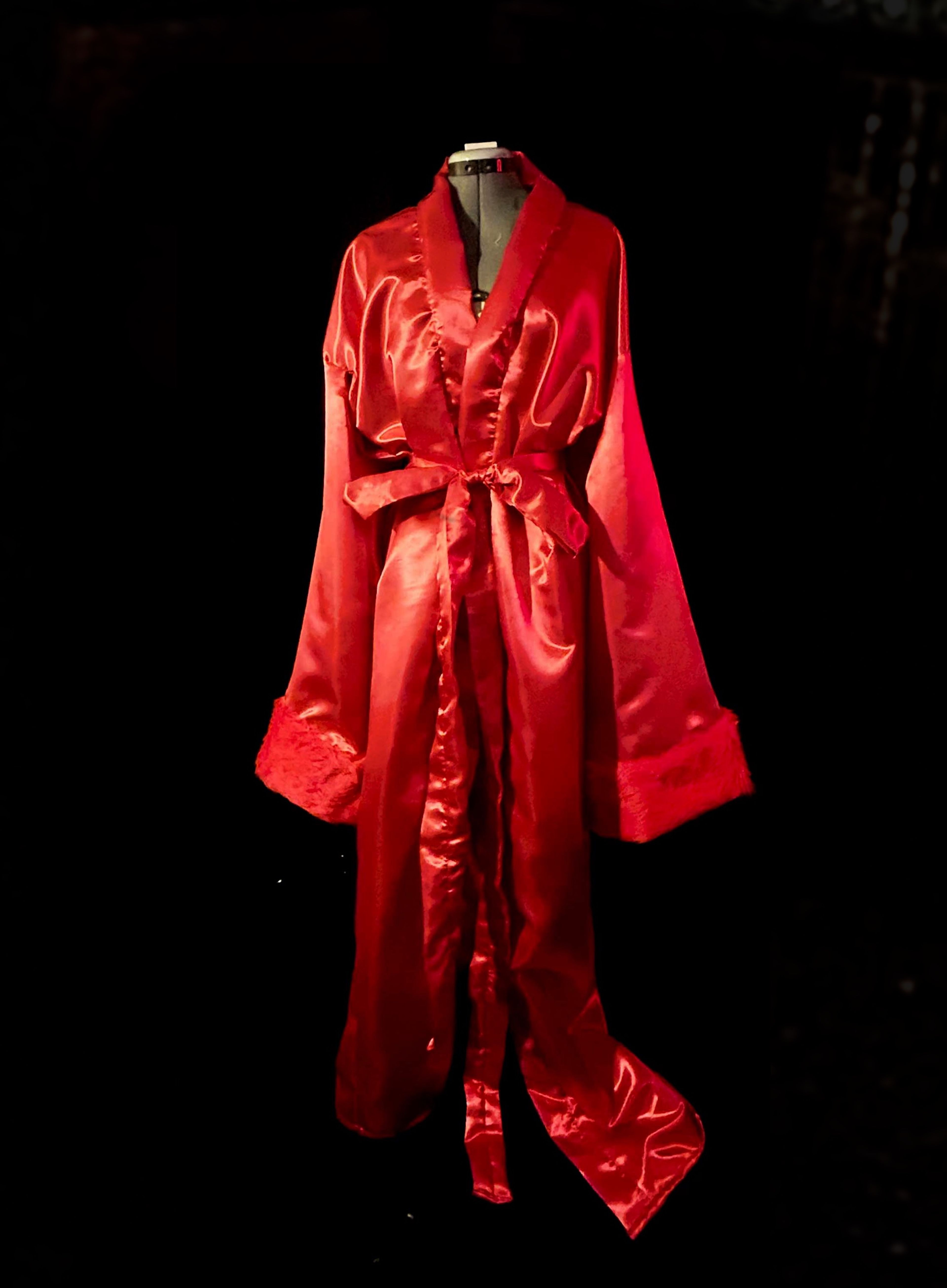 A long, red satin robe on a mannequin, featuring a waist tie and wide sleeves with textured cuffs.