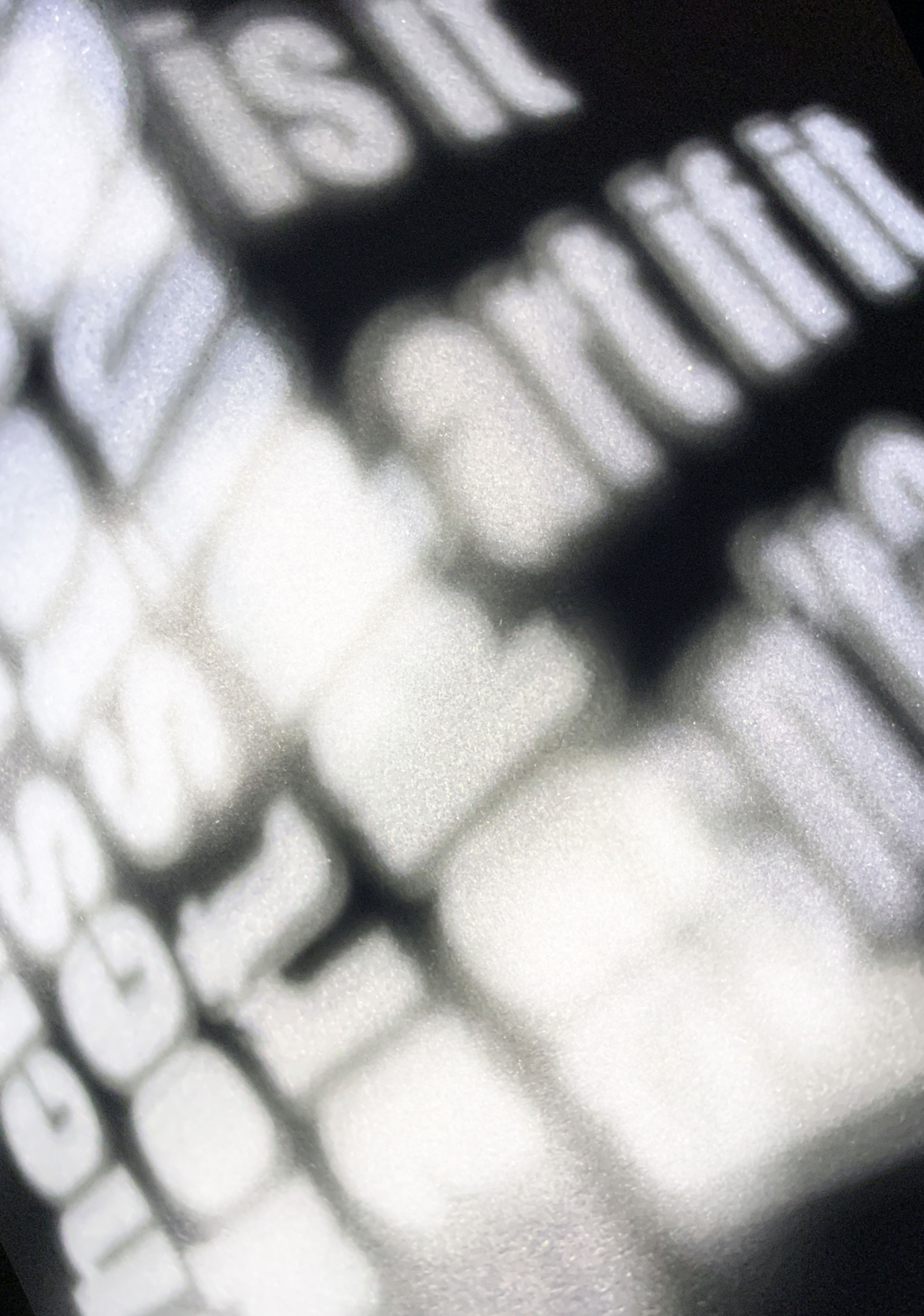 Abstract shadow of white text projected onto a surface, out of focus, creating a moody and ethereal effect. The text is not fully legible, adding a layer of mystery and ambiguity.