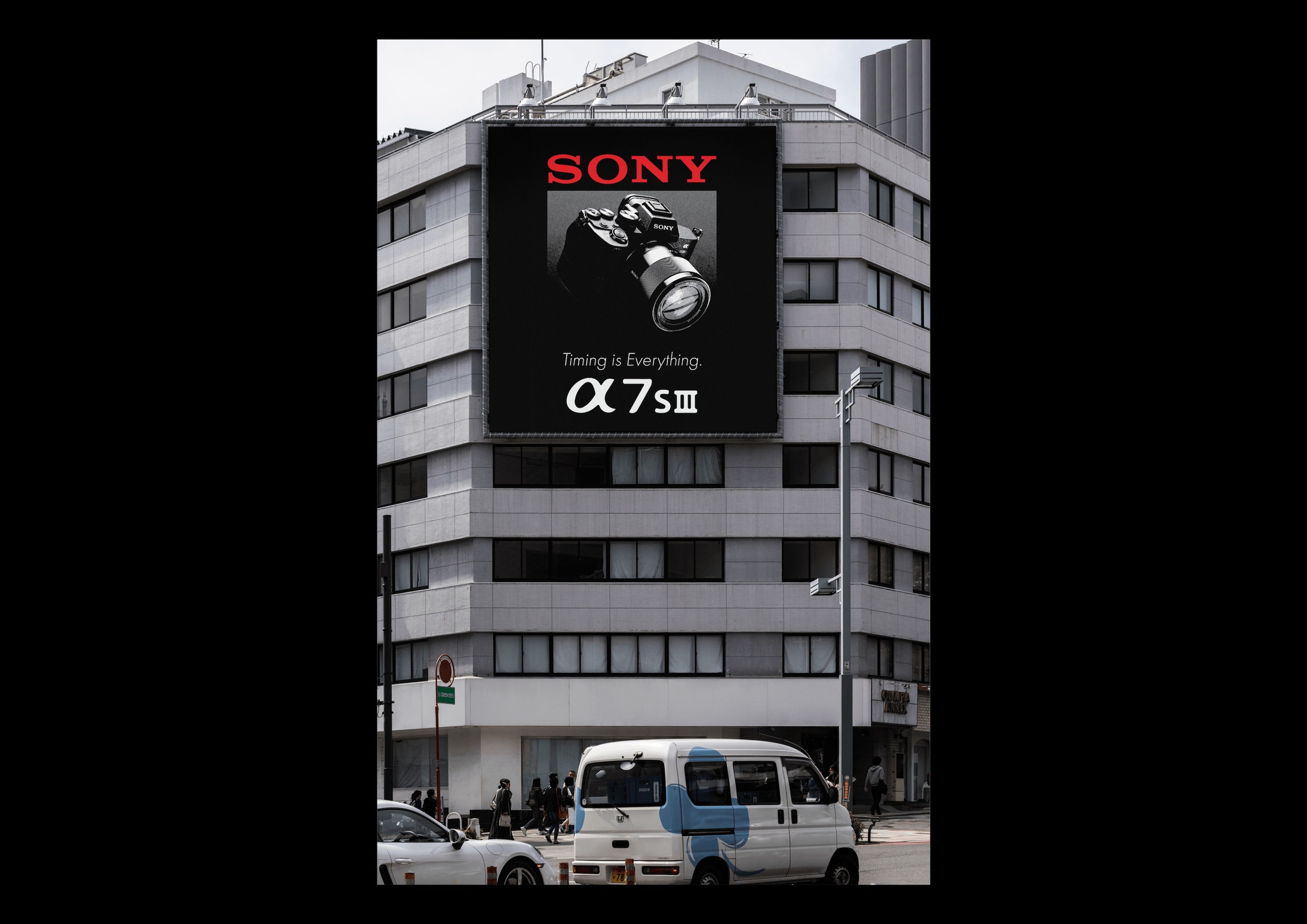 A building facade with a large billboard advertisement for Sony, featuring a close-up image of a camera and the text "Sony Alpha 7S III" with the tagline "Timing is Everything." Pedestrians and a vehicle are visible below the sign.