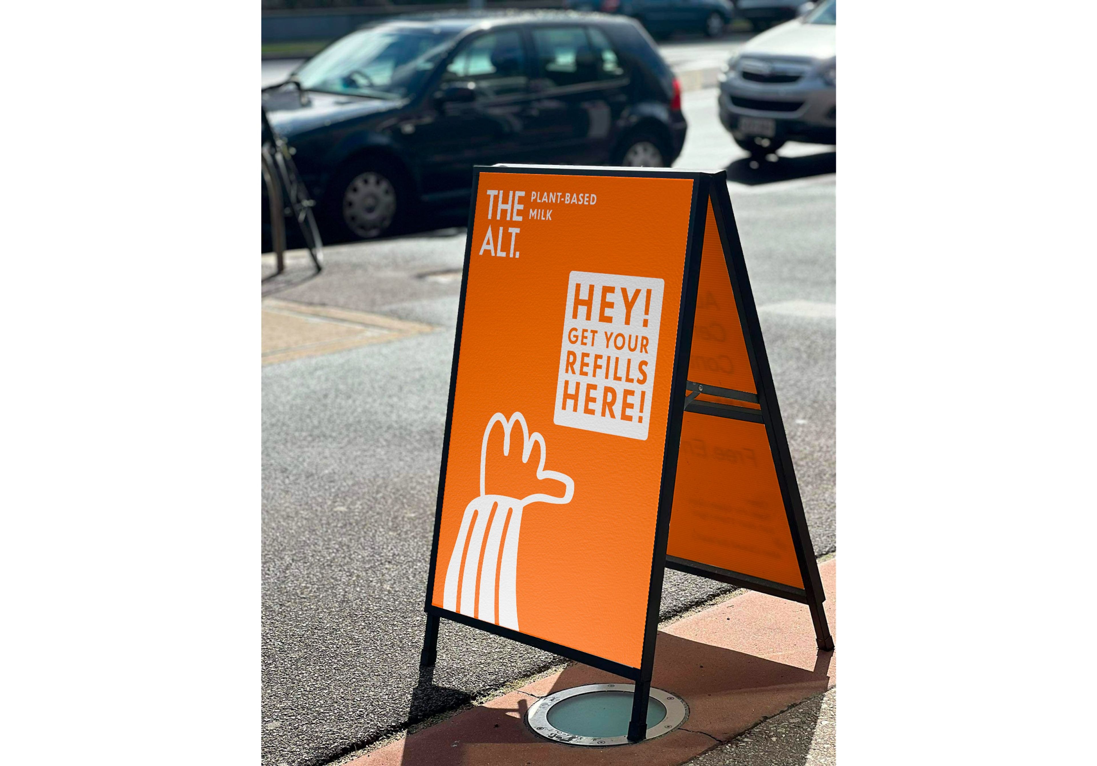 A-frame sidewalk sign for 'THE ALT' plant-based milk in vibrant orange, featuring minimalist white illustrations and bold typography announcing 'HEY! GET YOUR REFILLS HERE!'