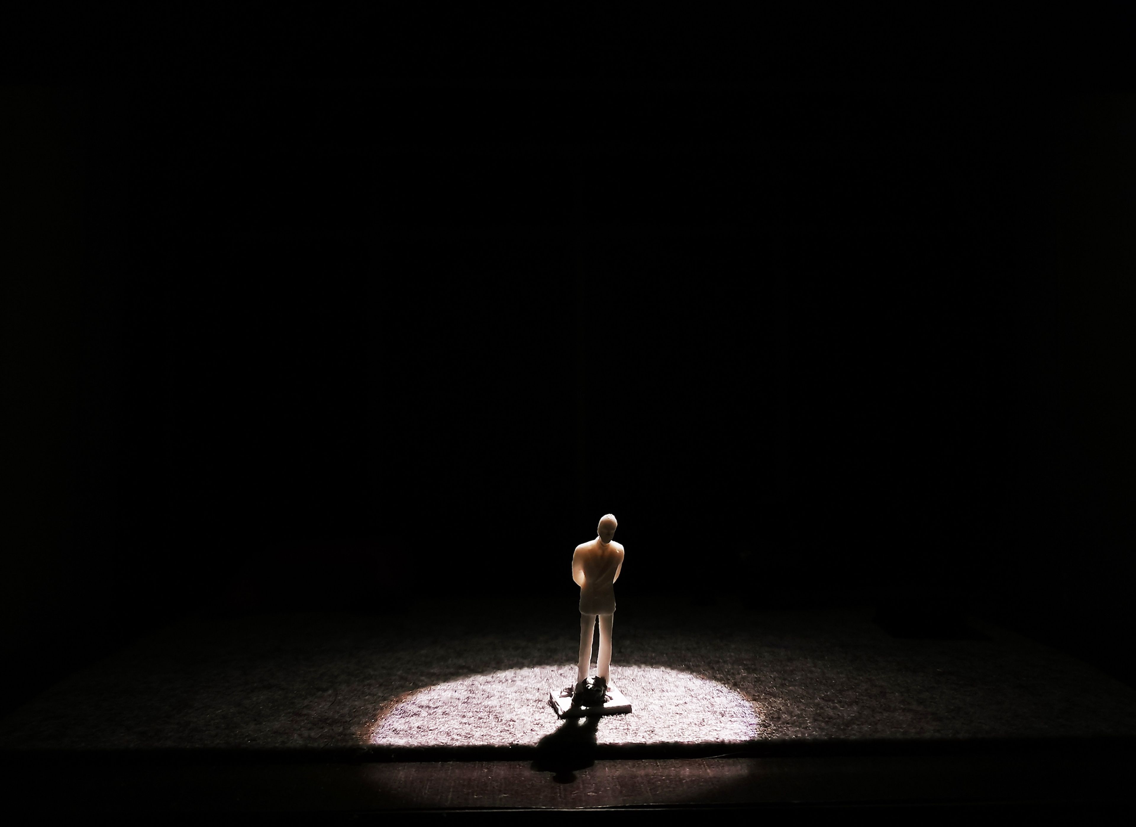 Scale model of a set design with a single spotlight focused on a figure standing alone in a dark space.