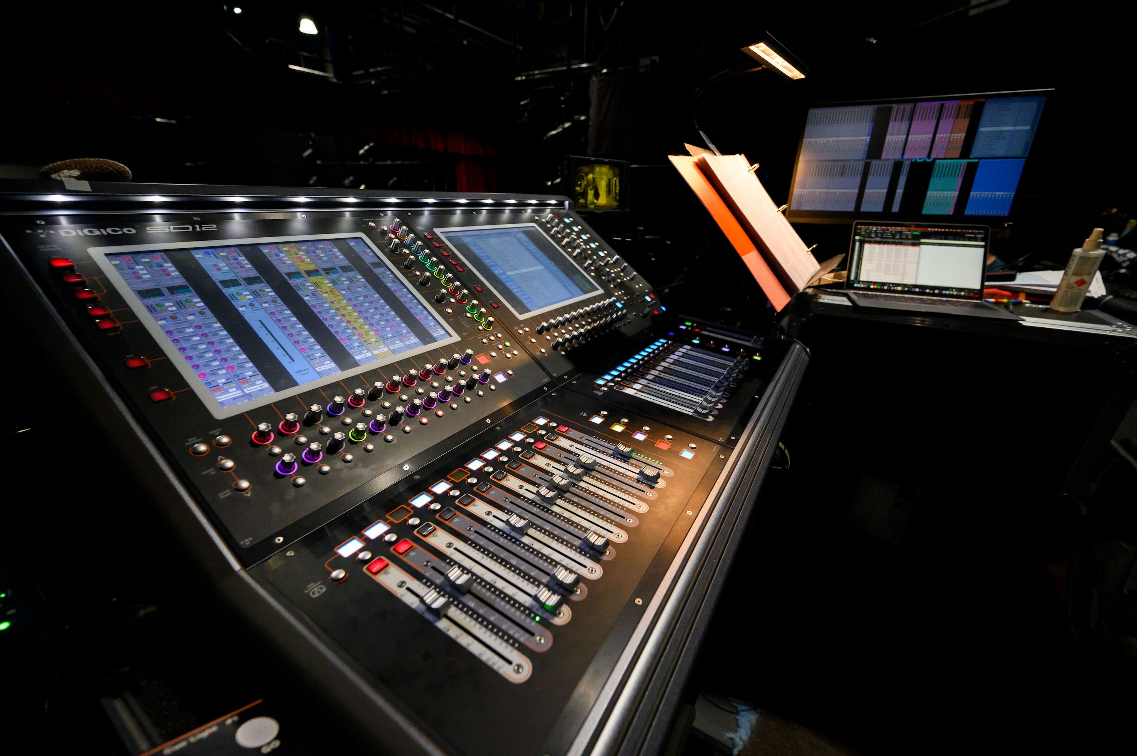 Close-up of a digital sound mixing console with colourful controls and screens displaying audio levels and settings.