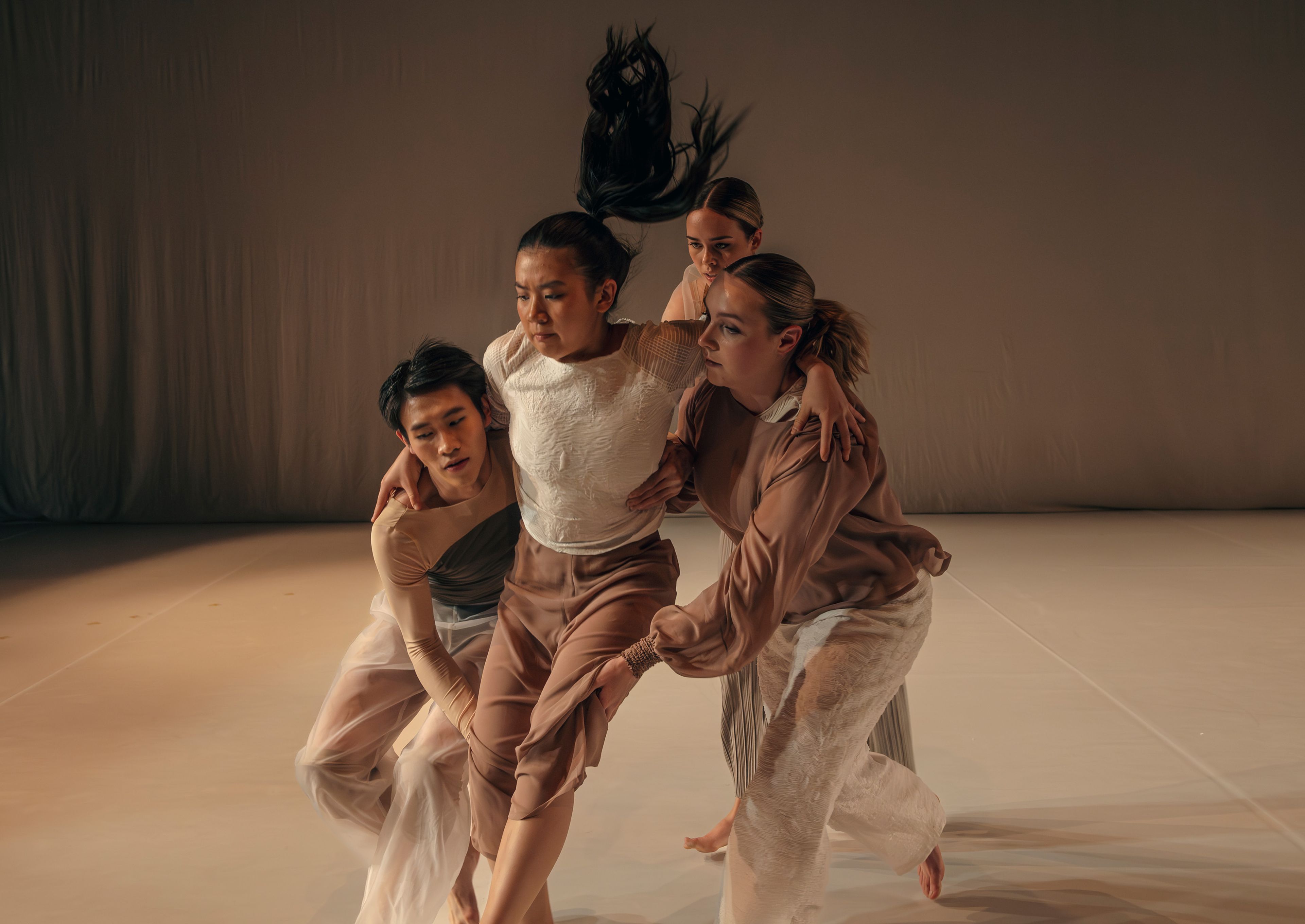 Dance production photograph with four dancers supporting another dancer in the centre, with warm, subdued lighting.