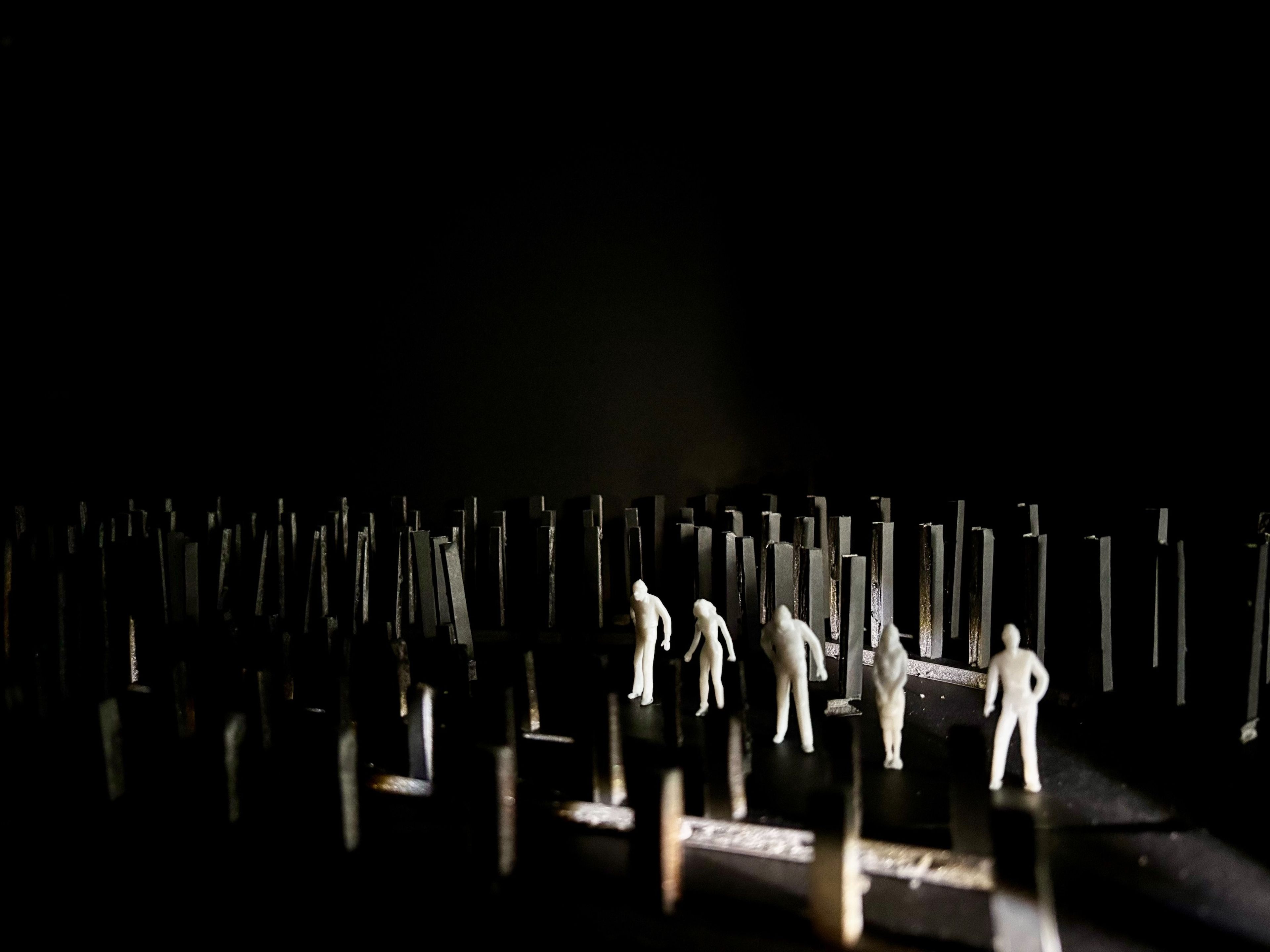 Six white figures standing amongst tall, black structures on a dark stage.